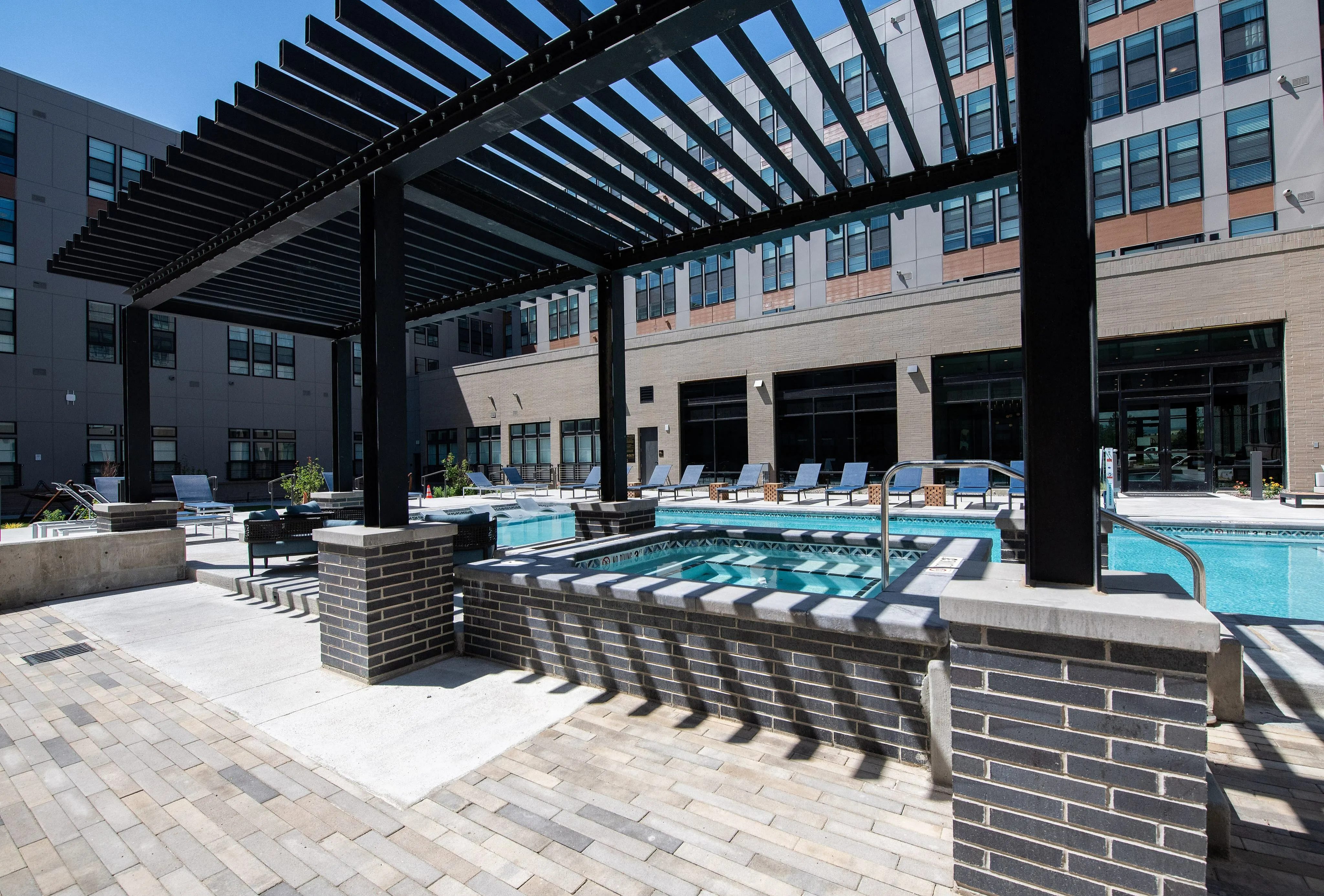 Luxurious apartment pool area featuring a modern pergola, stylish poolside seating, and sleek architectural elements.
