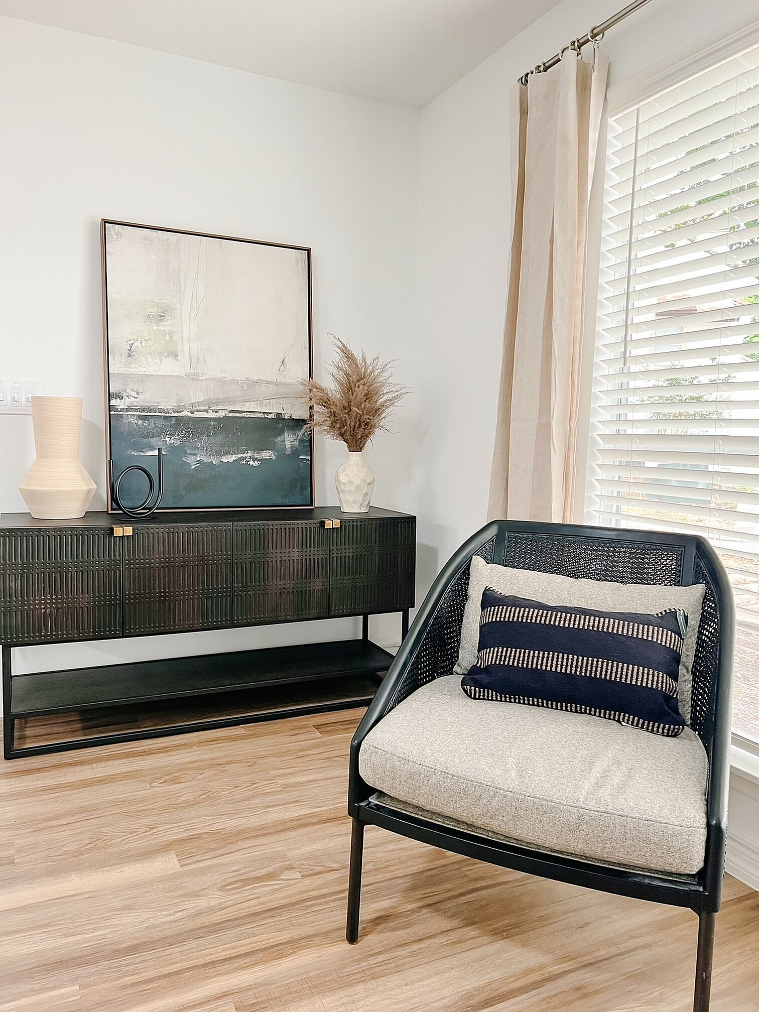 Chic living space with elegant decor, featuring a modern black chair, stylish console, and artistic wall painting, complemented by natural light.