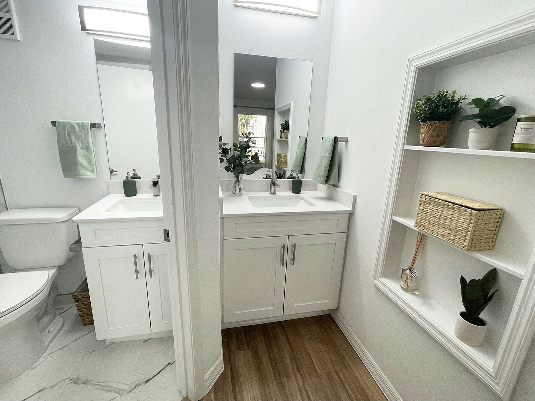 Bright and modern bathroom with dual sinks, elegant white cabinetry, and stylish shelving with decor for a refreshing ambiance.