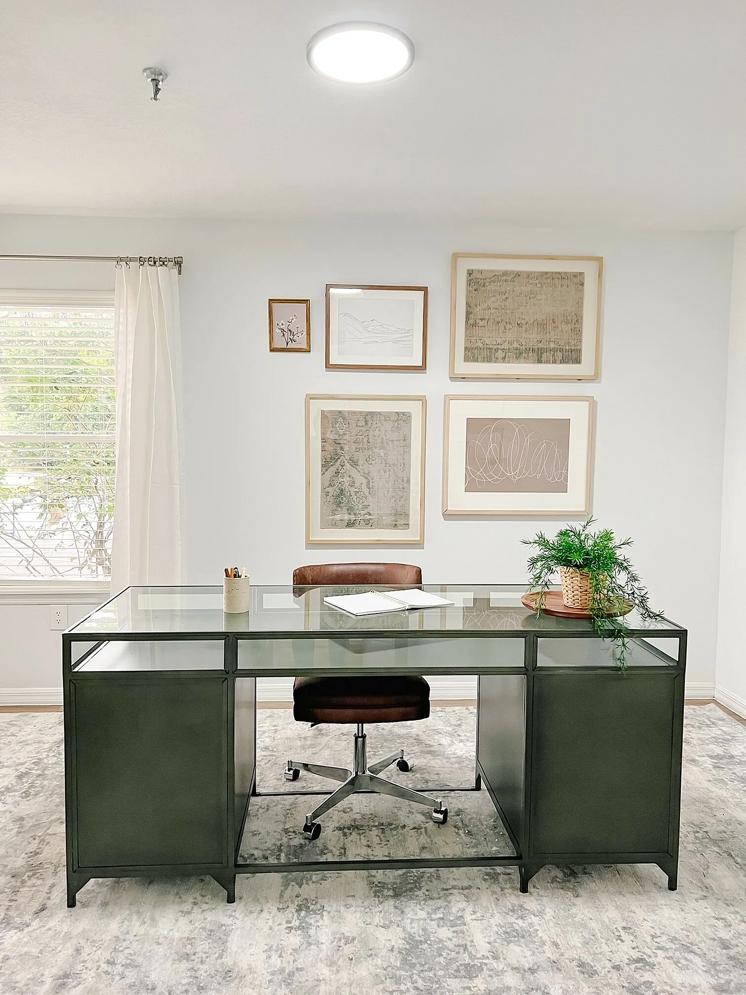 Elegant home office with a sleek glass desk, stylish brown chair, and artistic wall gallery, offering a serene workspace atmosphere.