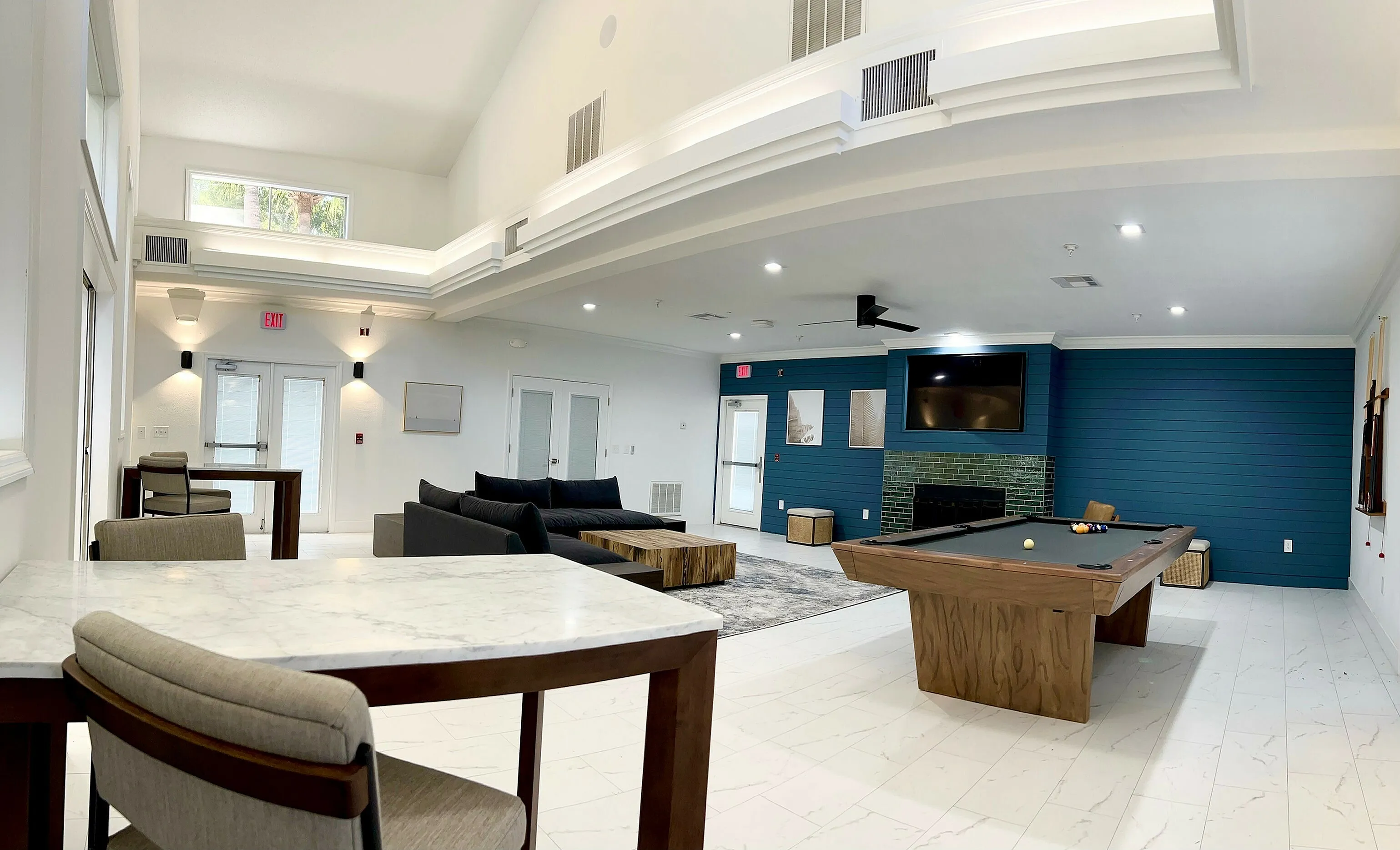 Modern lounge area featuring high ceilings, a stylish pool table, comfortable seating, and an inviting fireplace.
