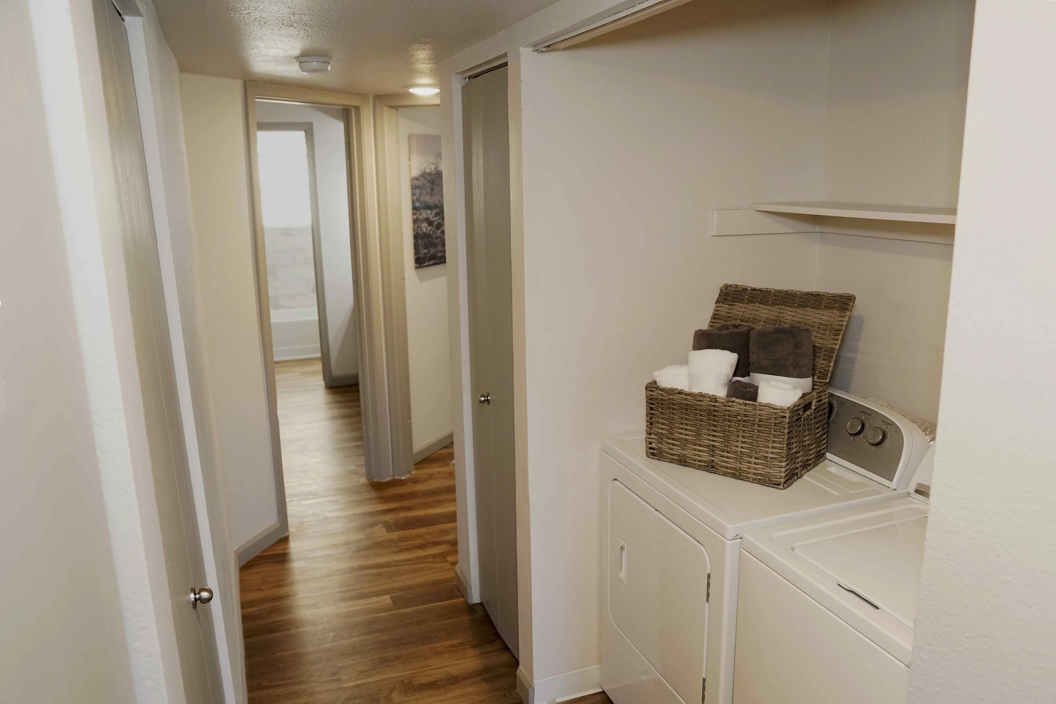 Inviting apartment hallway leading to a modern bathroom, featuring elegant wood flooring and a convenient laundry area with stylish storage.