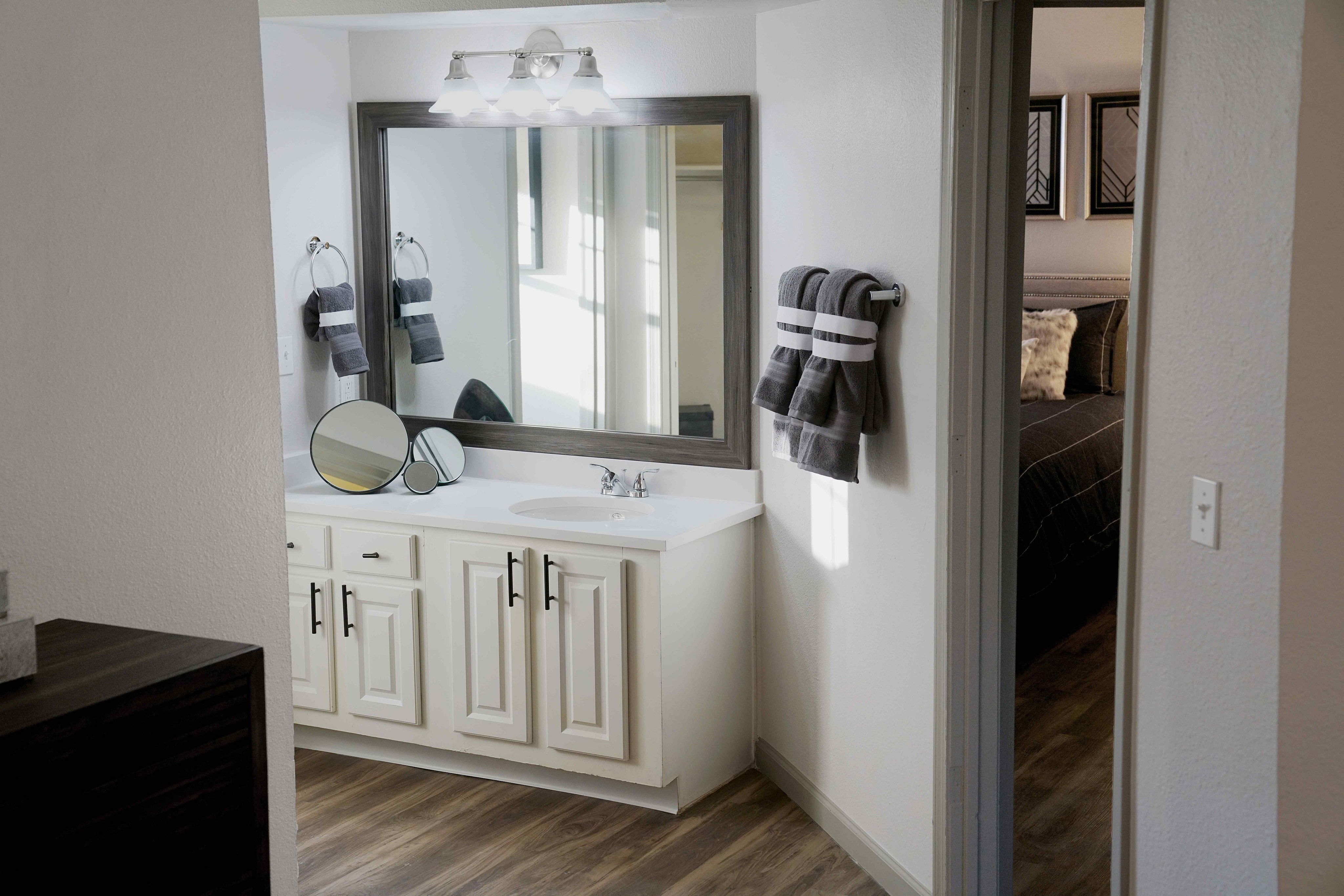 Elegant bathroom with a large mirror, modern vanity, and plush towels, leading to a cozy bedroom with stylish decor.