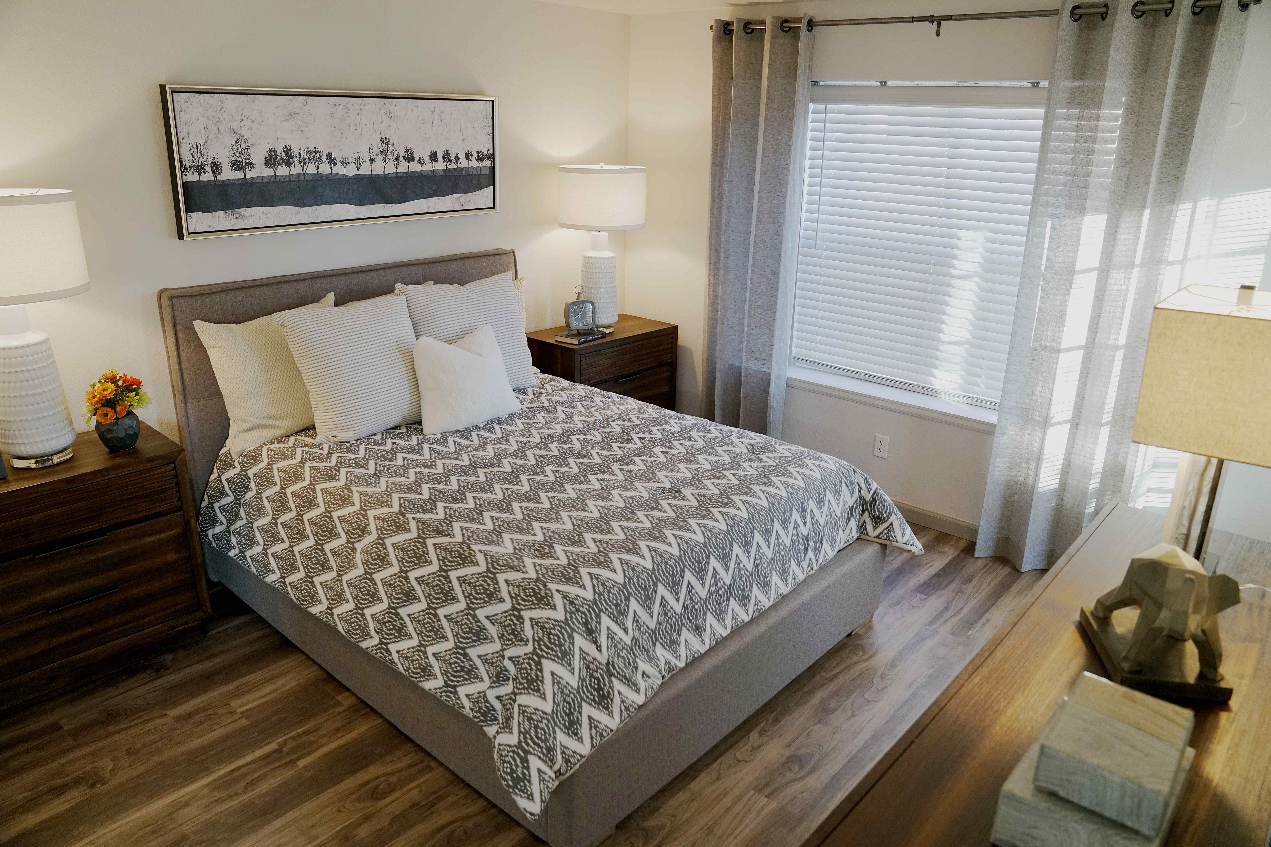 Inviting bedroom with chic decor, featuring a cozy bed, elegant artwork, and soft natural light streaming through sheer curtains.