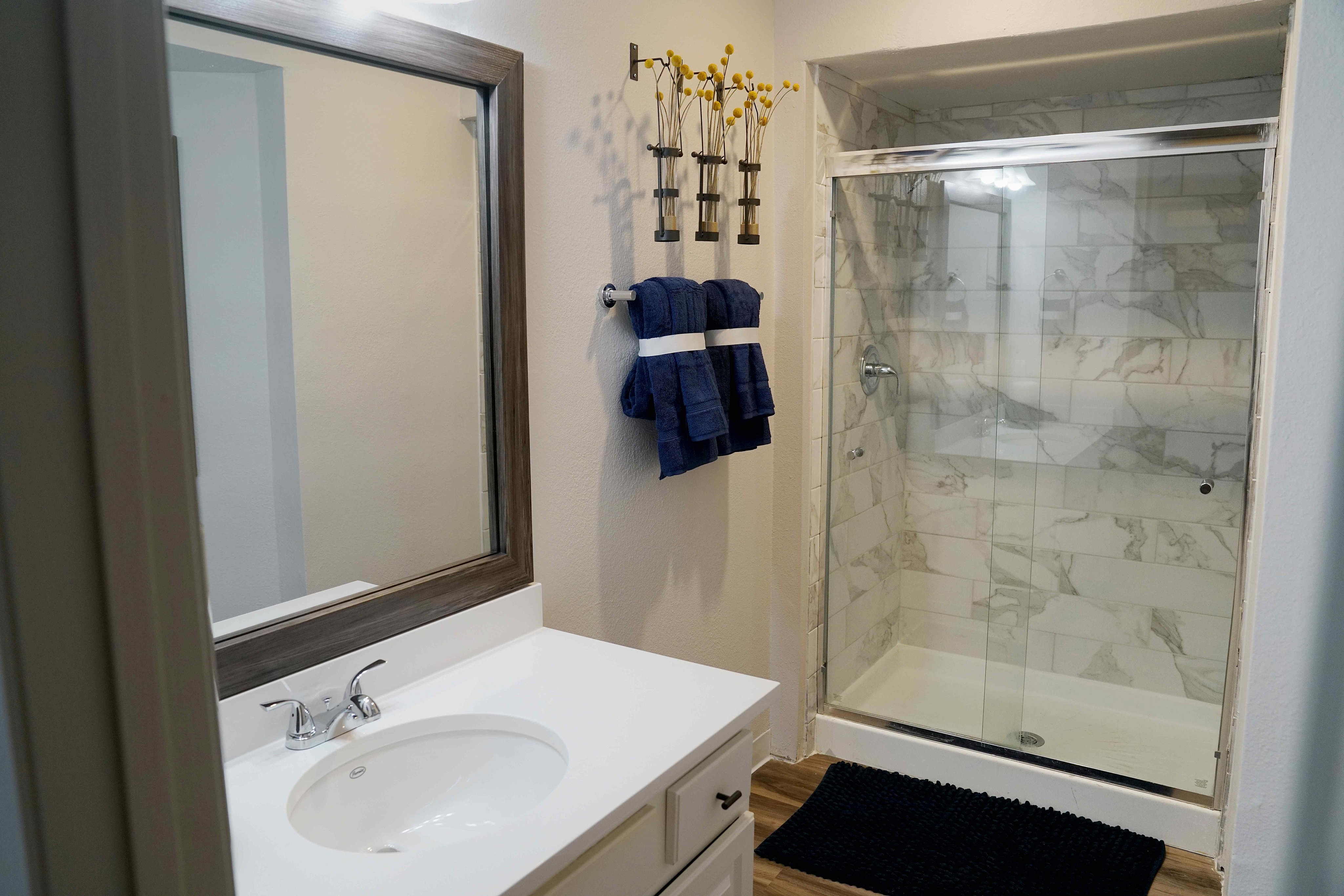 Elegant bathroom with a sleek marble-tiled shower, large mirror, and stylish modern sink.