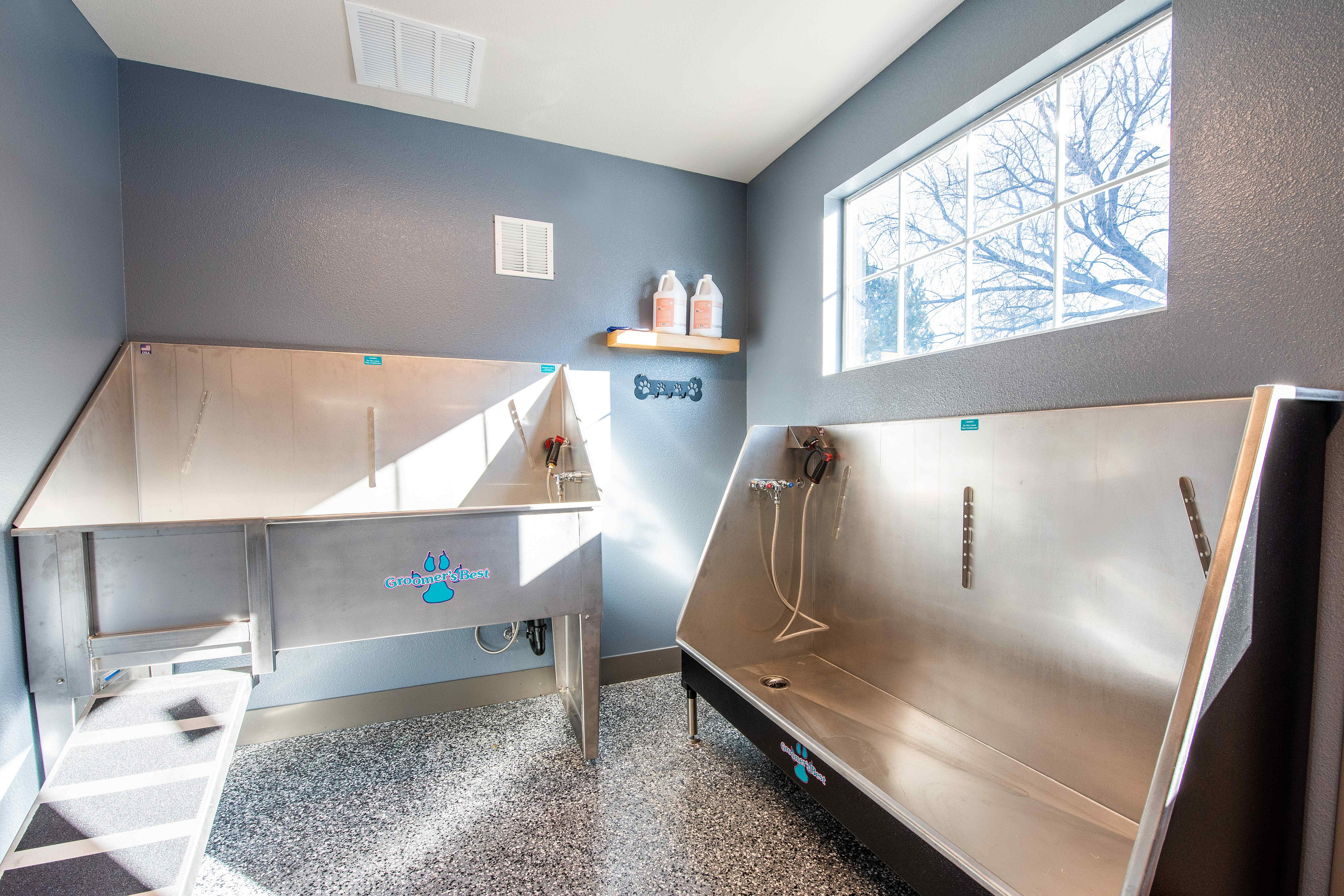 Bright and spacious pet grooming station with stainless steel wash tubs, modern fixtures, and large window offering natural light.