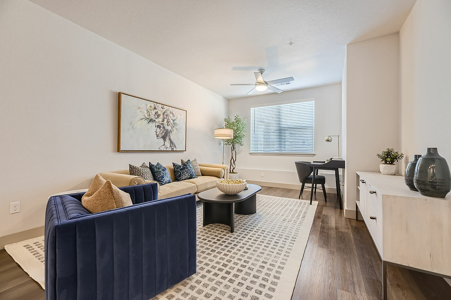 Inviting living room with elegant decor, featuring a plush blue and beige sofa set, modern artwork, and natural light streaming through a window.