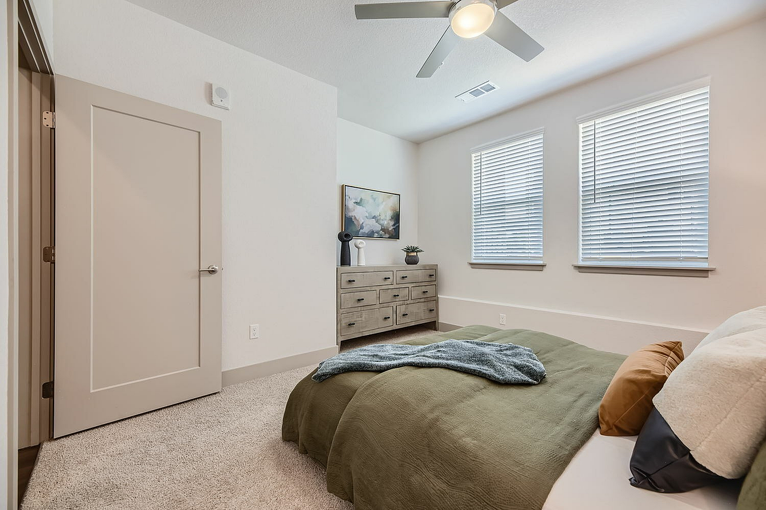 Inviting bedroom with modern decor, featuring a plush bed, elegant dresser, and ample natural light from large windows.