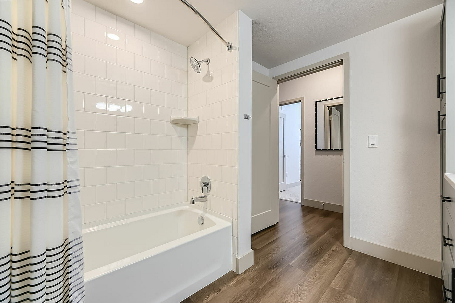 Inviting bathroom with elegant white tiles, a chic shower and tub combo, and stylish wood flooring, creating a serene oasis.