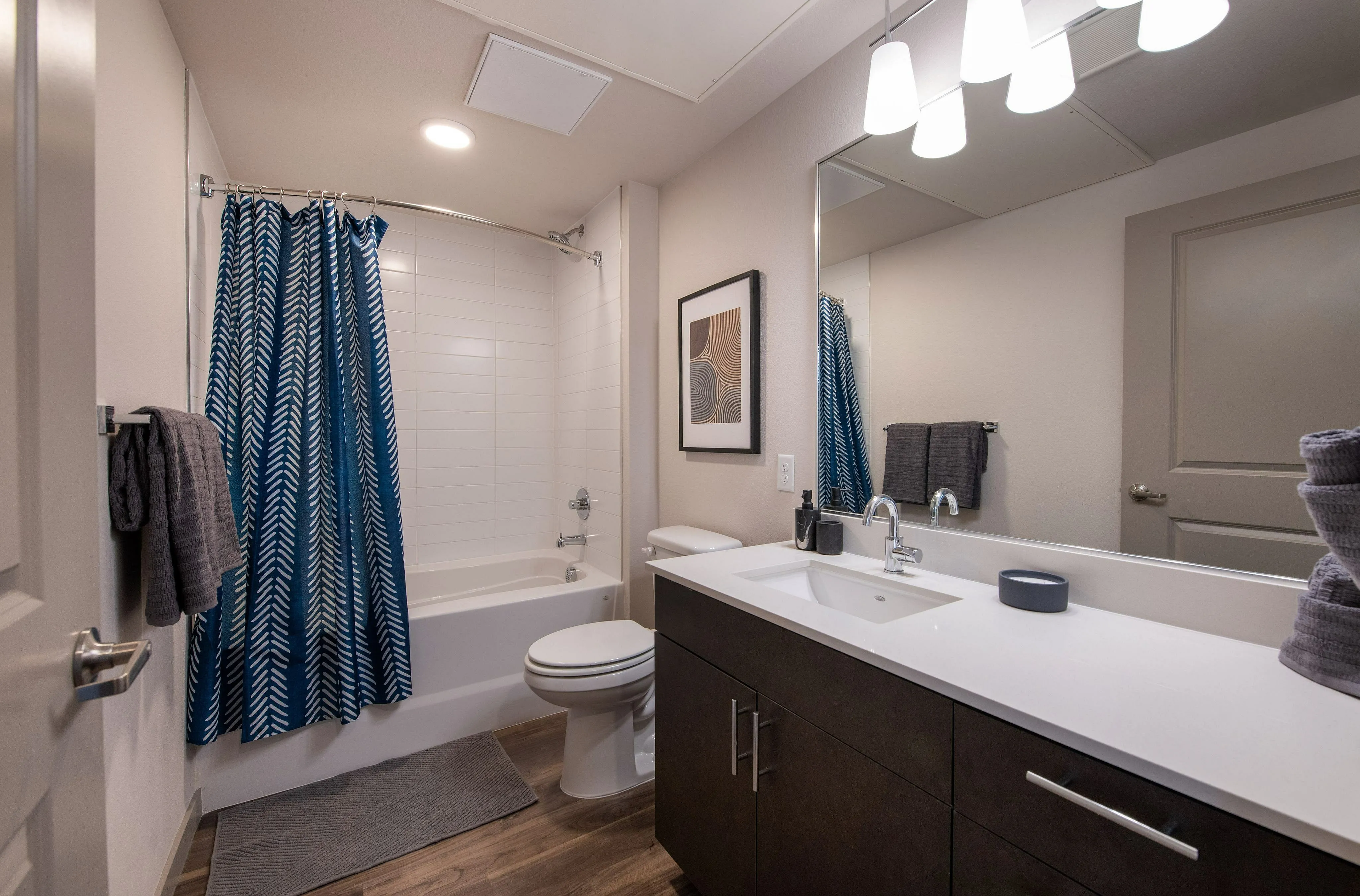 Modern bathroom with elegant dark wood vanity, stylish lighting, and a chic blue and white shower curtain.