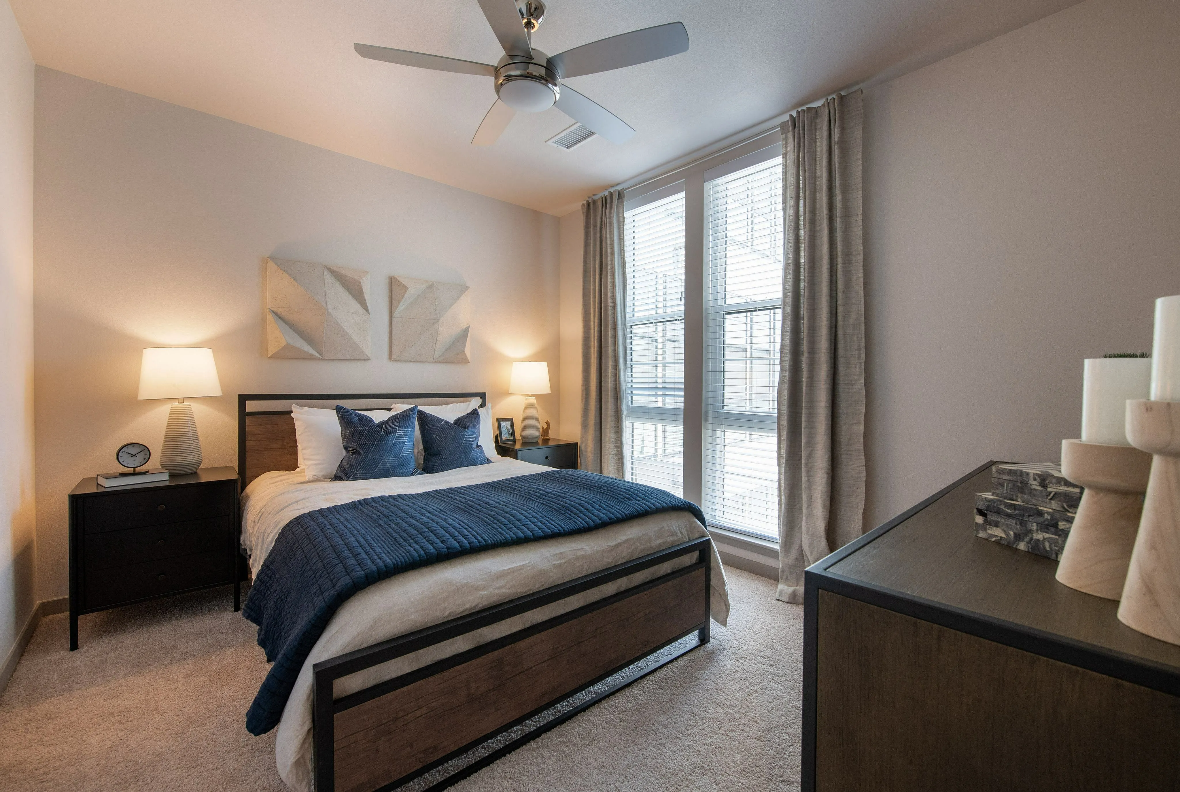 Elegant bedroom with modern decor, featuring a cozy bed, stylish nightstands, and large windows with sheer curtains.