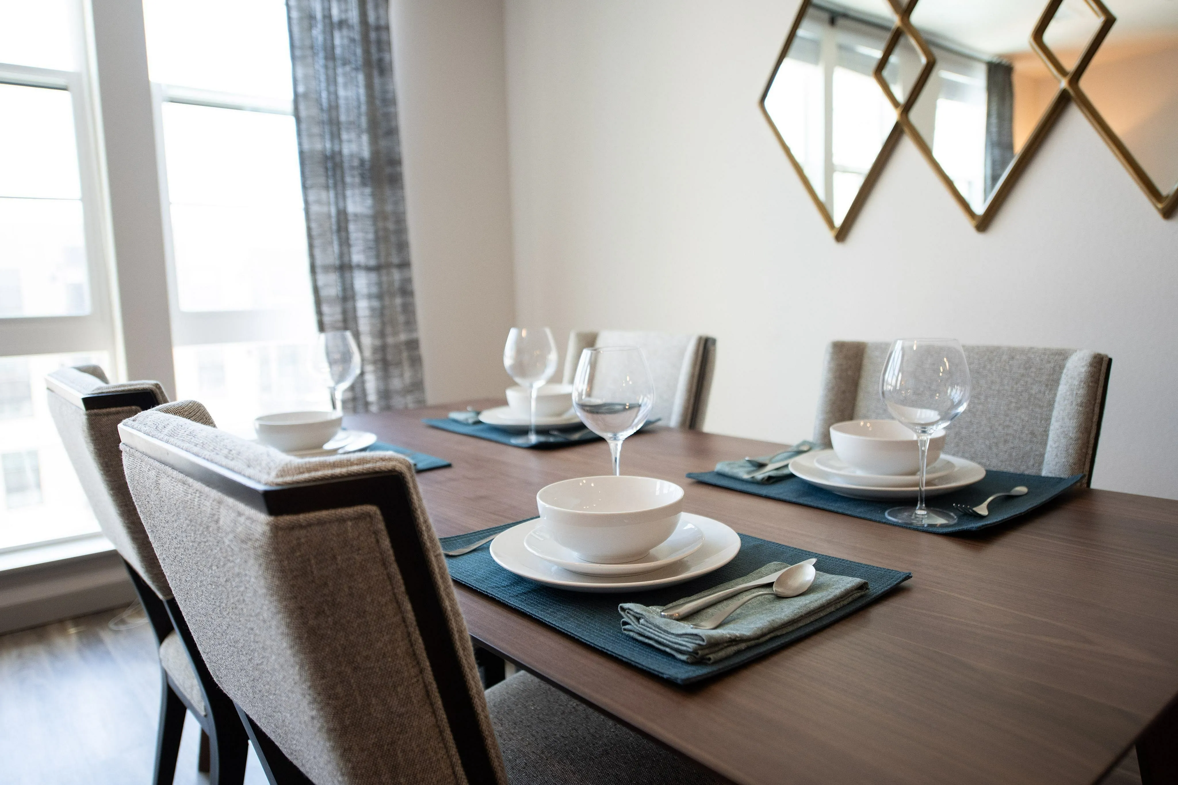 Elegant dining area with a modern table set for four, featuring polished wood furniture, stylish tableware, and natural light from large windows.