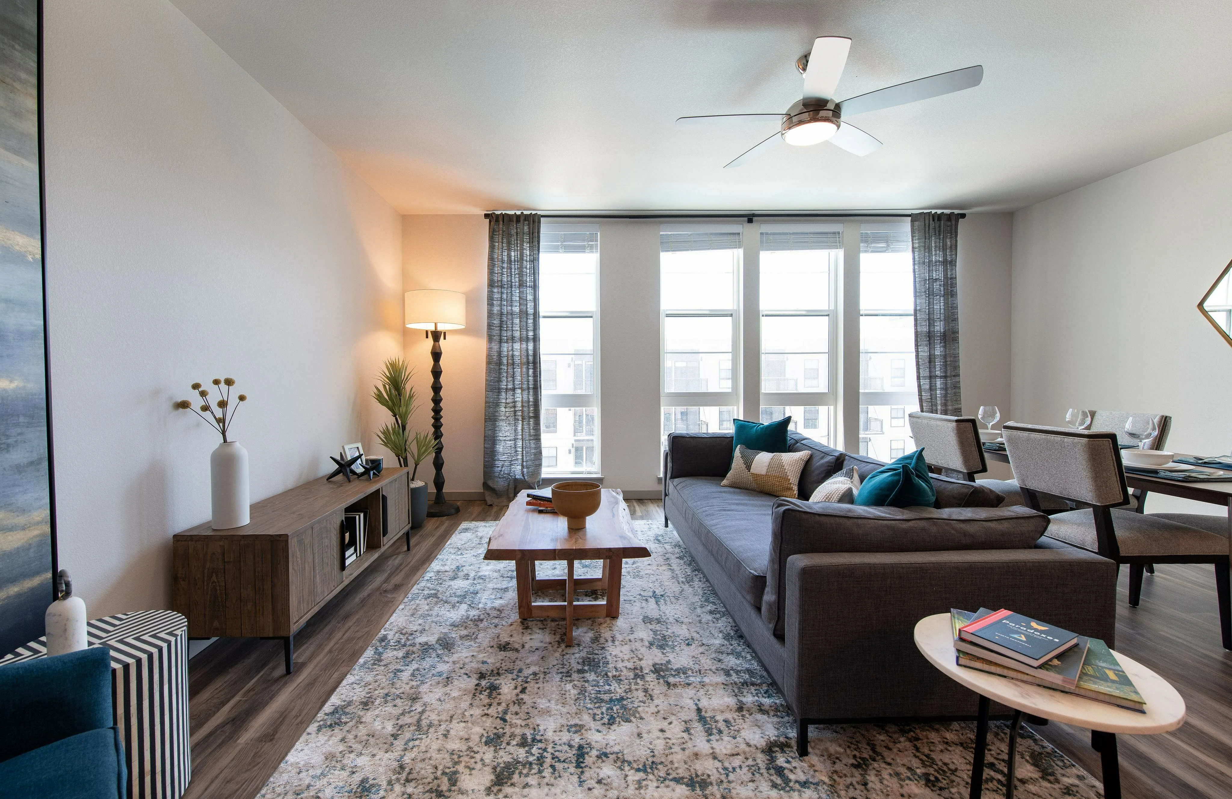 Chic modern living room with large windows, elegant decor, and a cozy dining area, offering ample natural light.
