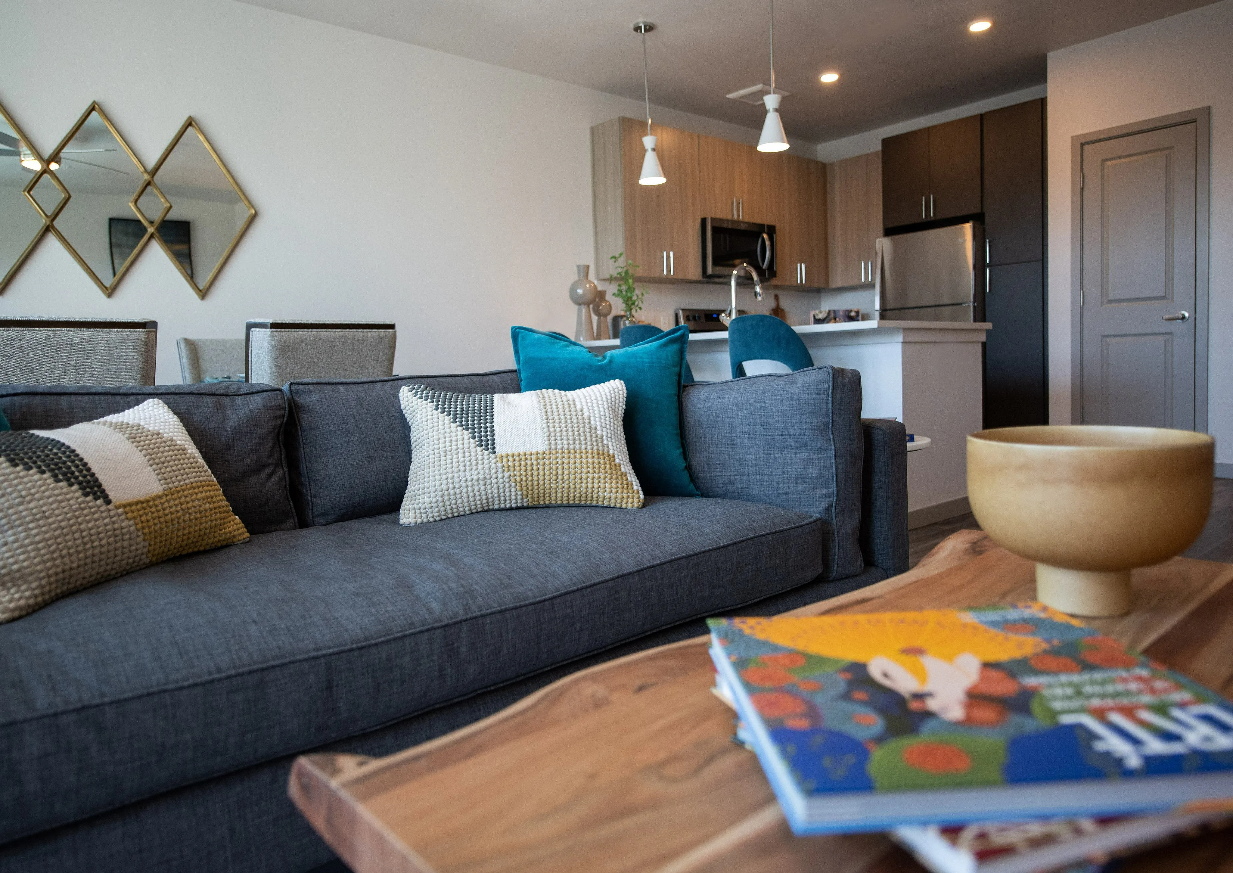 Inviting living space with modern open kitchen, plush gray sofa, vibrant cushions, and elegant wood accents creating a cozy atmosphere.