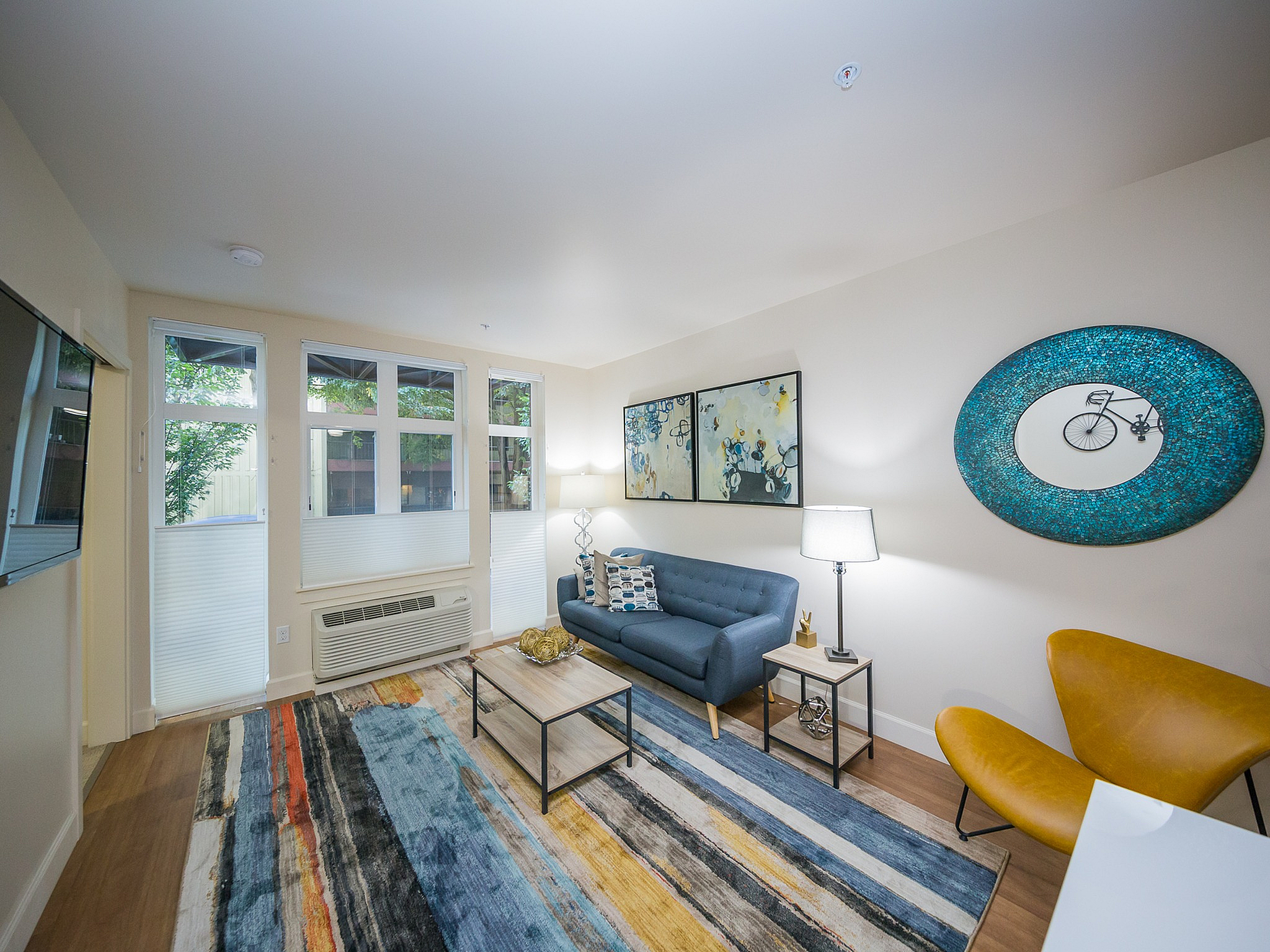 Contemporary living room with abundant natural light, featuring a cozy blue sofa, vibrant artwork, and a stylish rug enhancing the space.