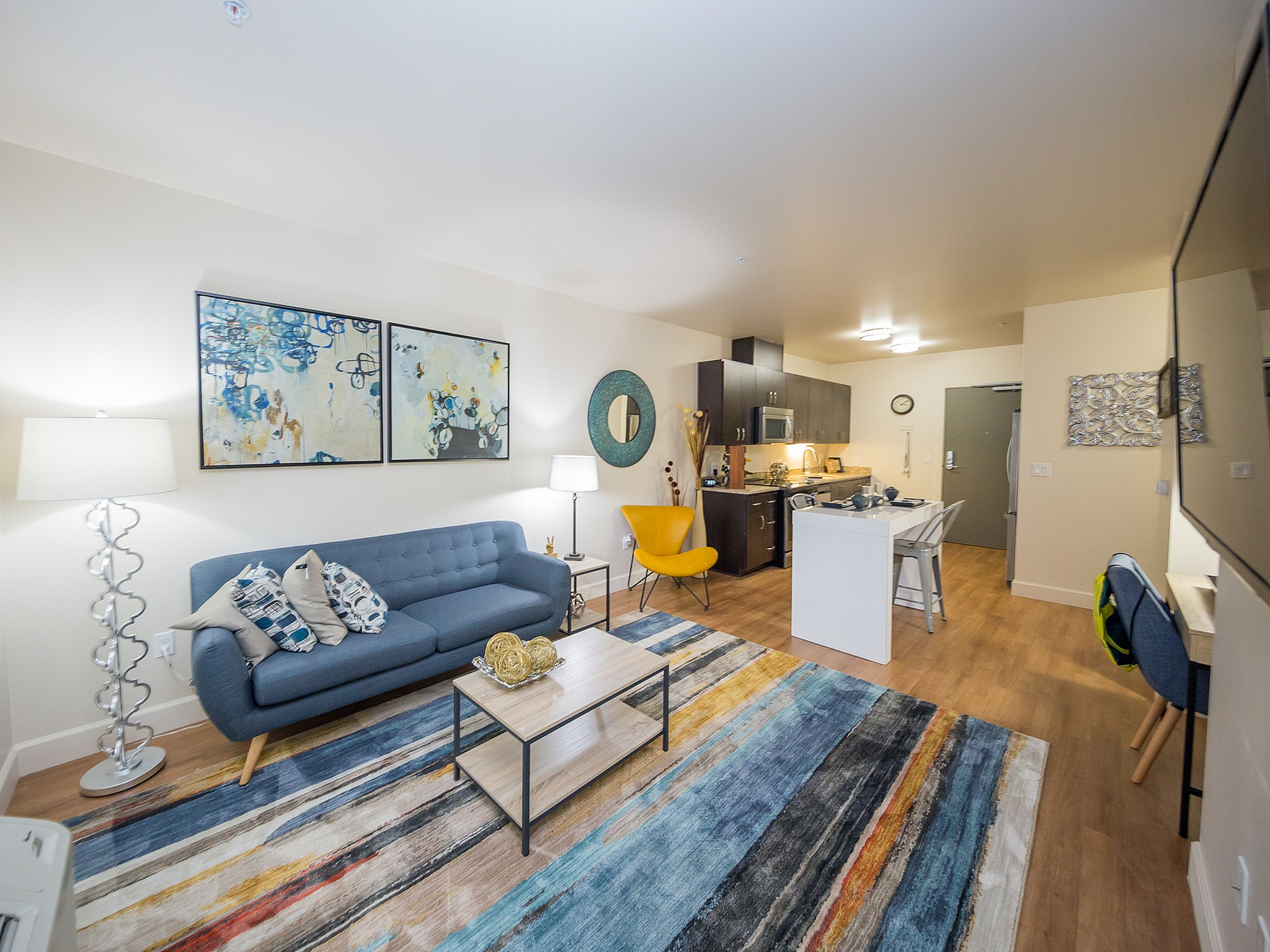 Modern open-concept living space with stylish decor, featuring a cozy blue sofa, vibrant artwork, and a sleek kitchen area.