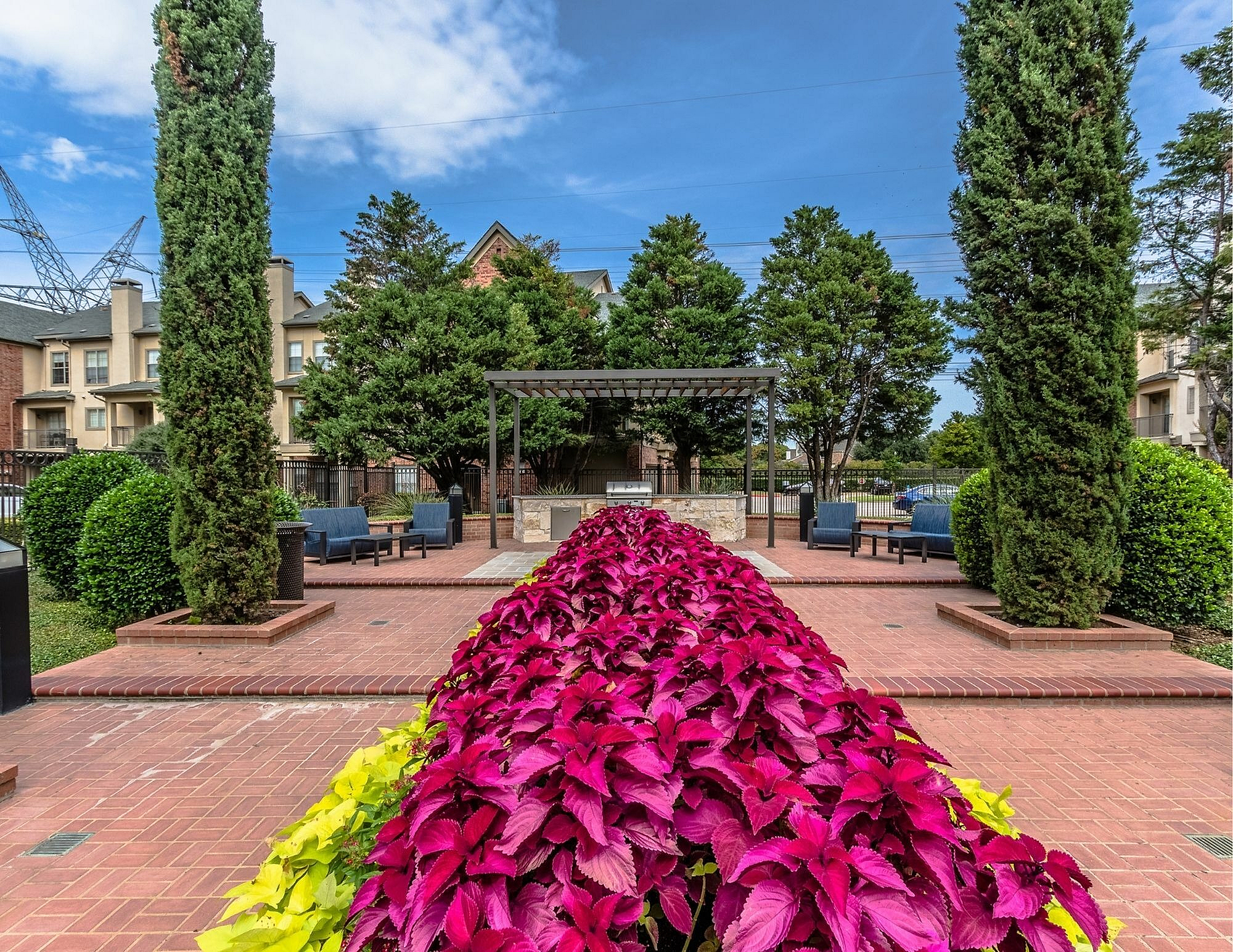 Charming outdoor community area with vibrant foliage, elegant brick pathways, and cozy seating under a stylish pergola.