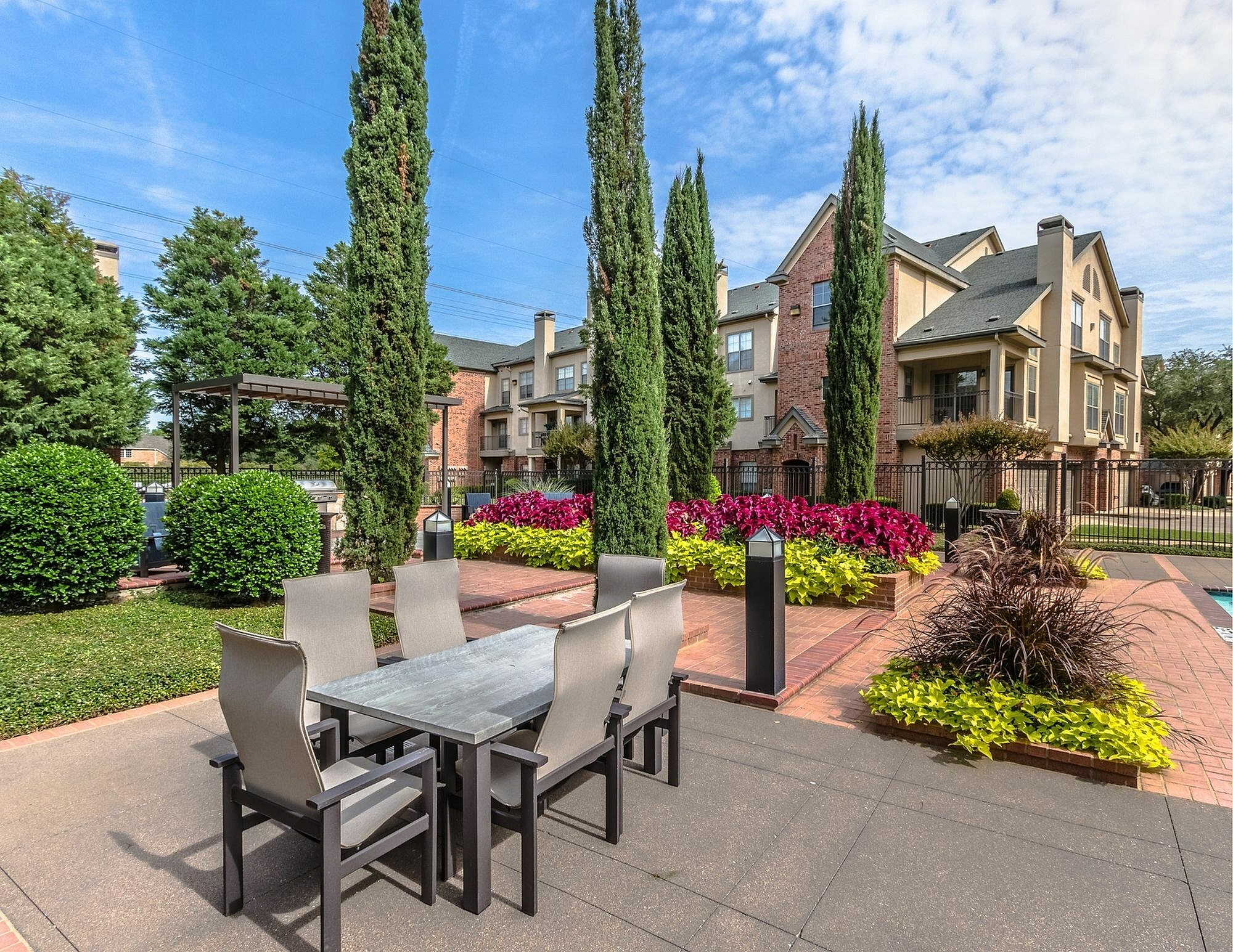 Elegant apartment exterior with lush landscaping, tall trees, and a stylish outdoor dining area.