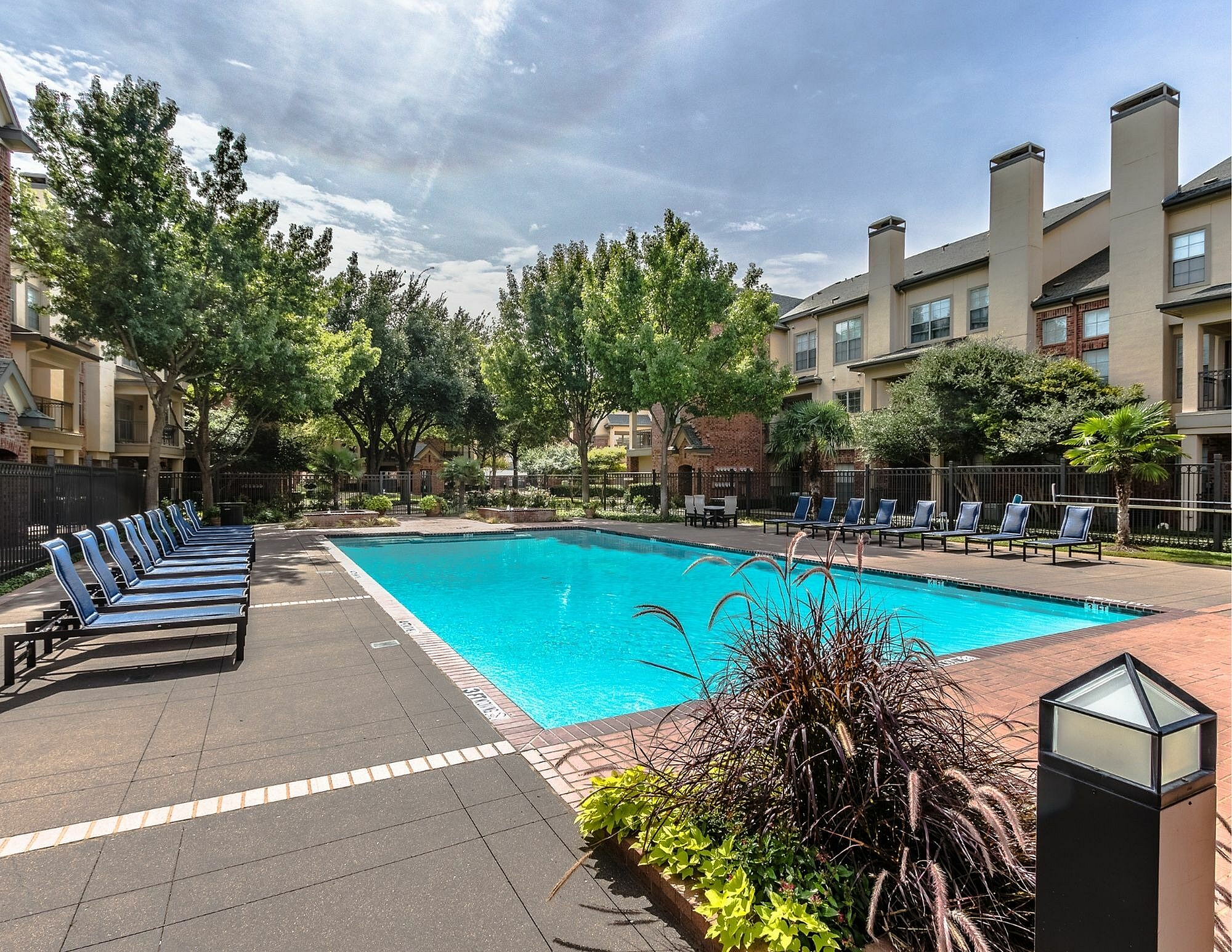 Luxurious apartment complex featuring a sparkling pool surrounded by elegant lounge chairs and lush greenery.