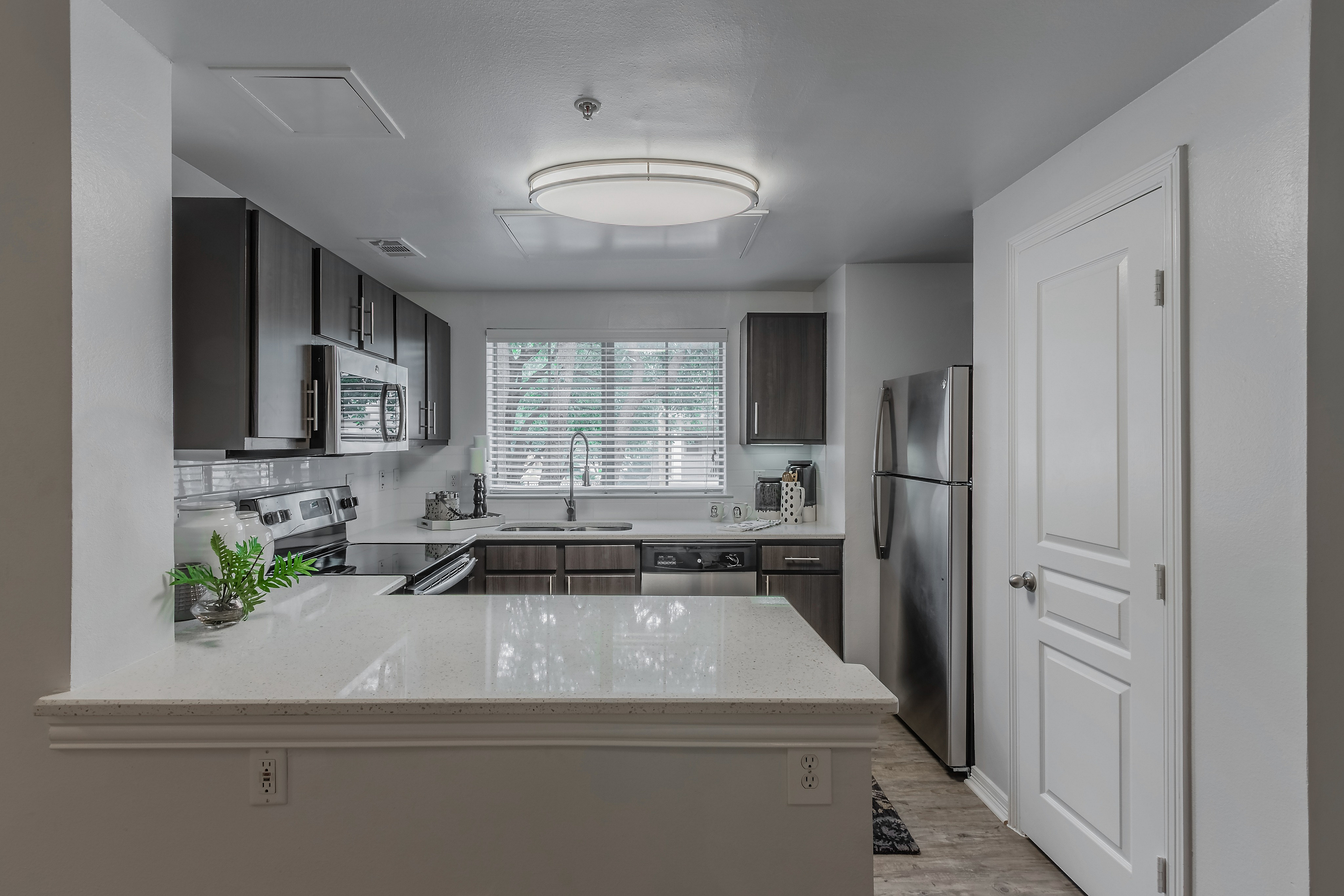Modern kitchen with sleek dark cabinets, stainless steel appliances, and a spacious countertop, accented by natural light through a large window.