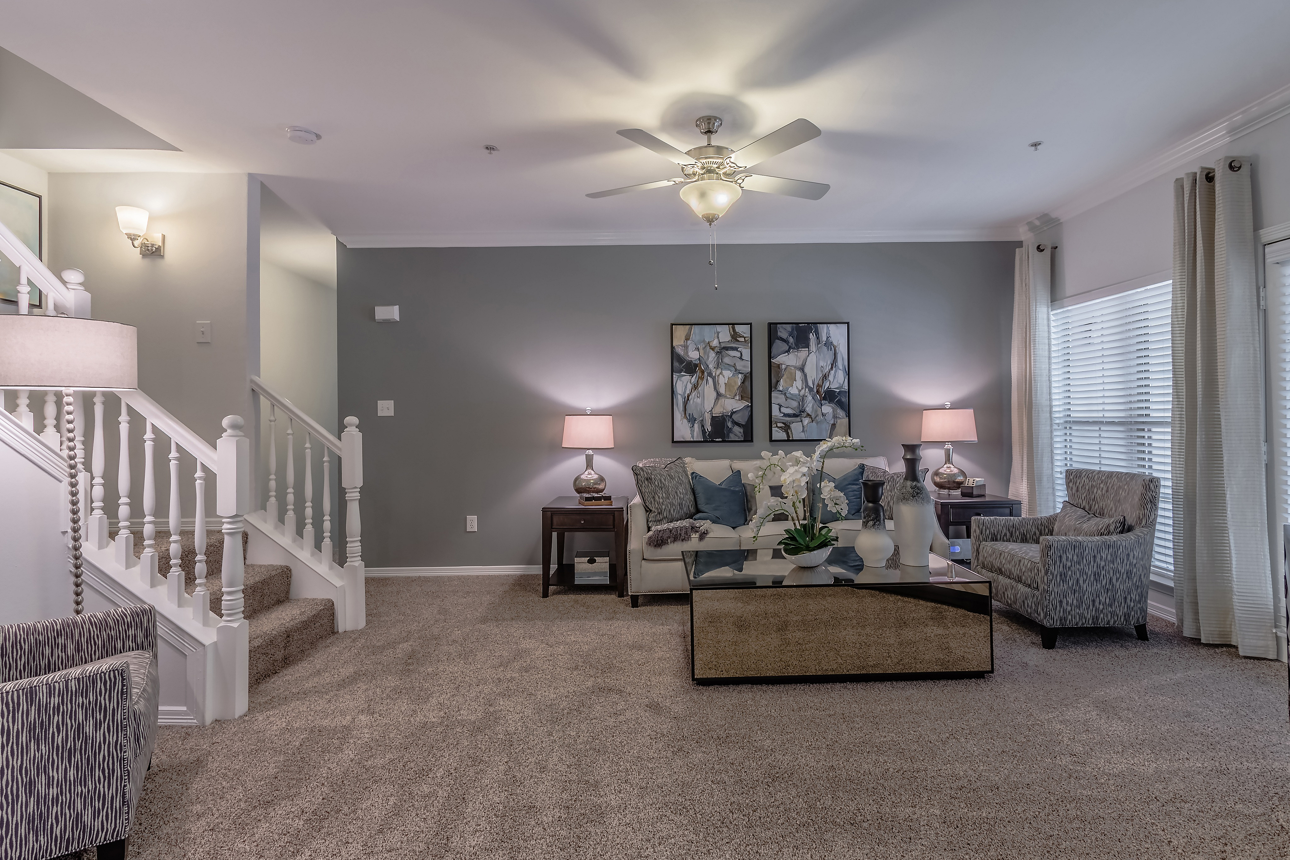 Chic living room with elegant decor, plush carpeting, stylish armchairs, and a modern staircase.