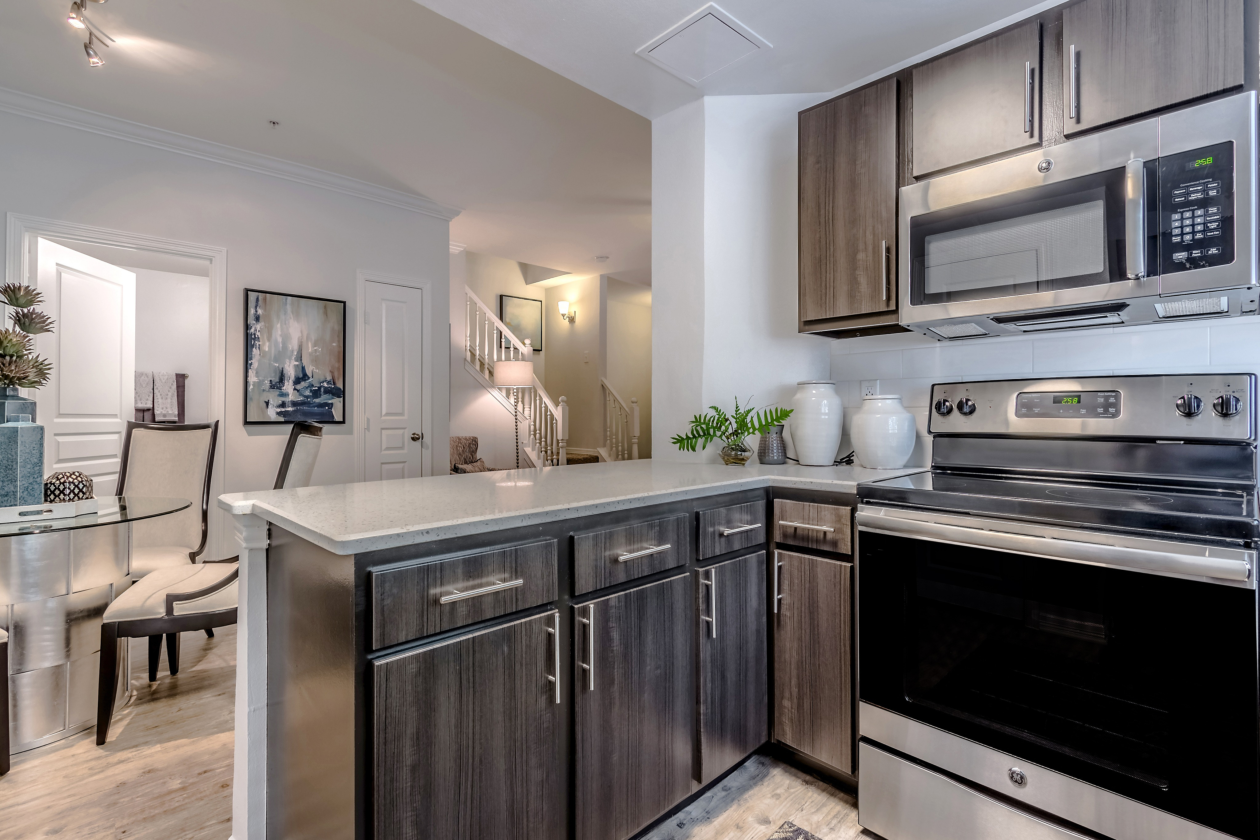 Modern kitchen with sleek stainless steel appliances, marble countertops, and warm wooden cabinetry, adjacent to open dining space with elegant chairs and artful decor.