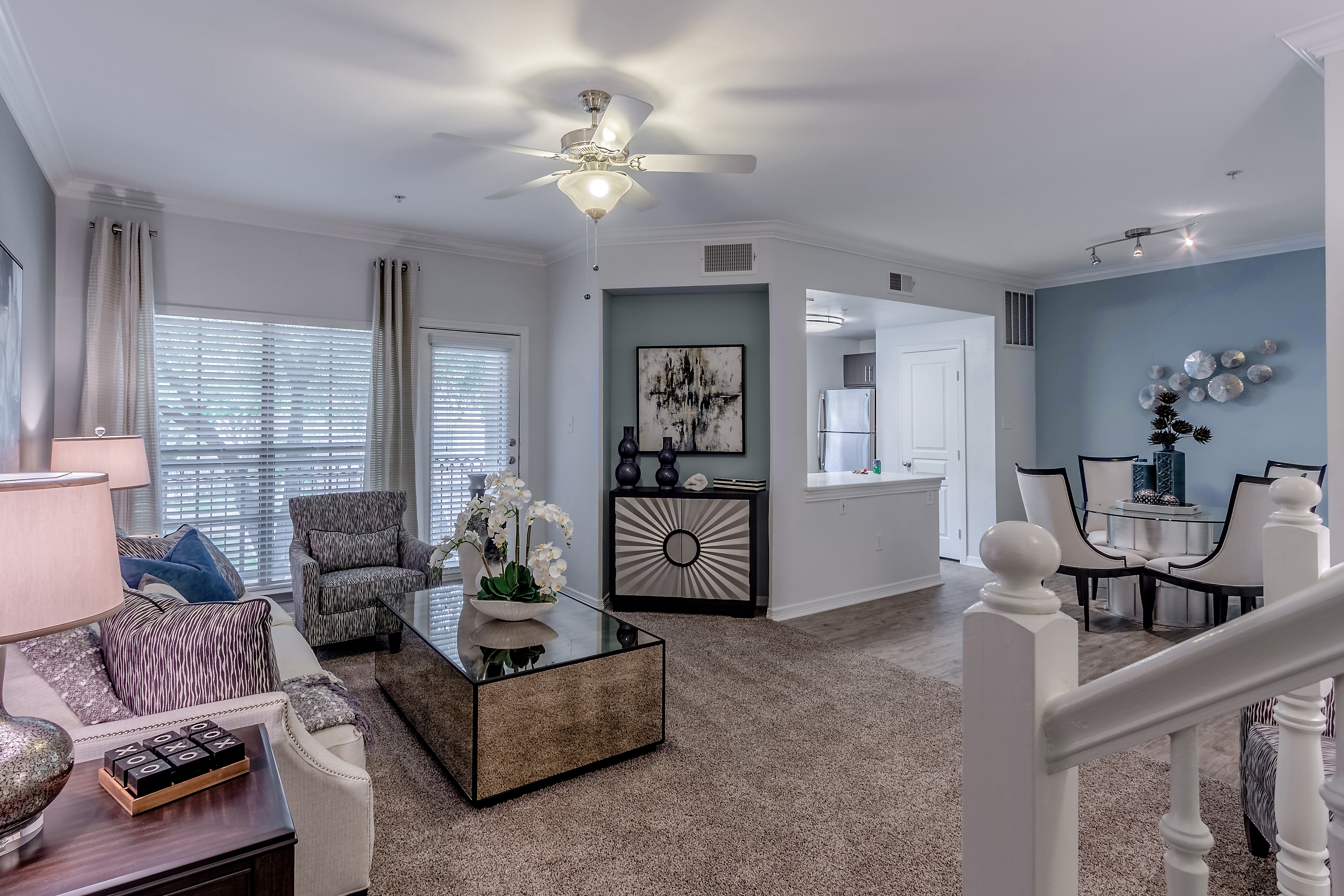 Elegant open-concept living room with cozy seating, sleek glass coffee table, and modern dining area. Bright kitchen view enhances the spacious ambiance.