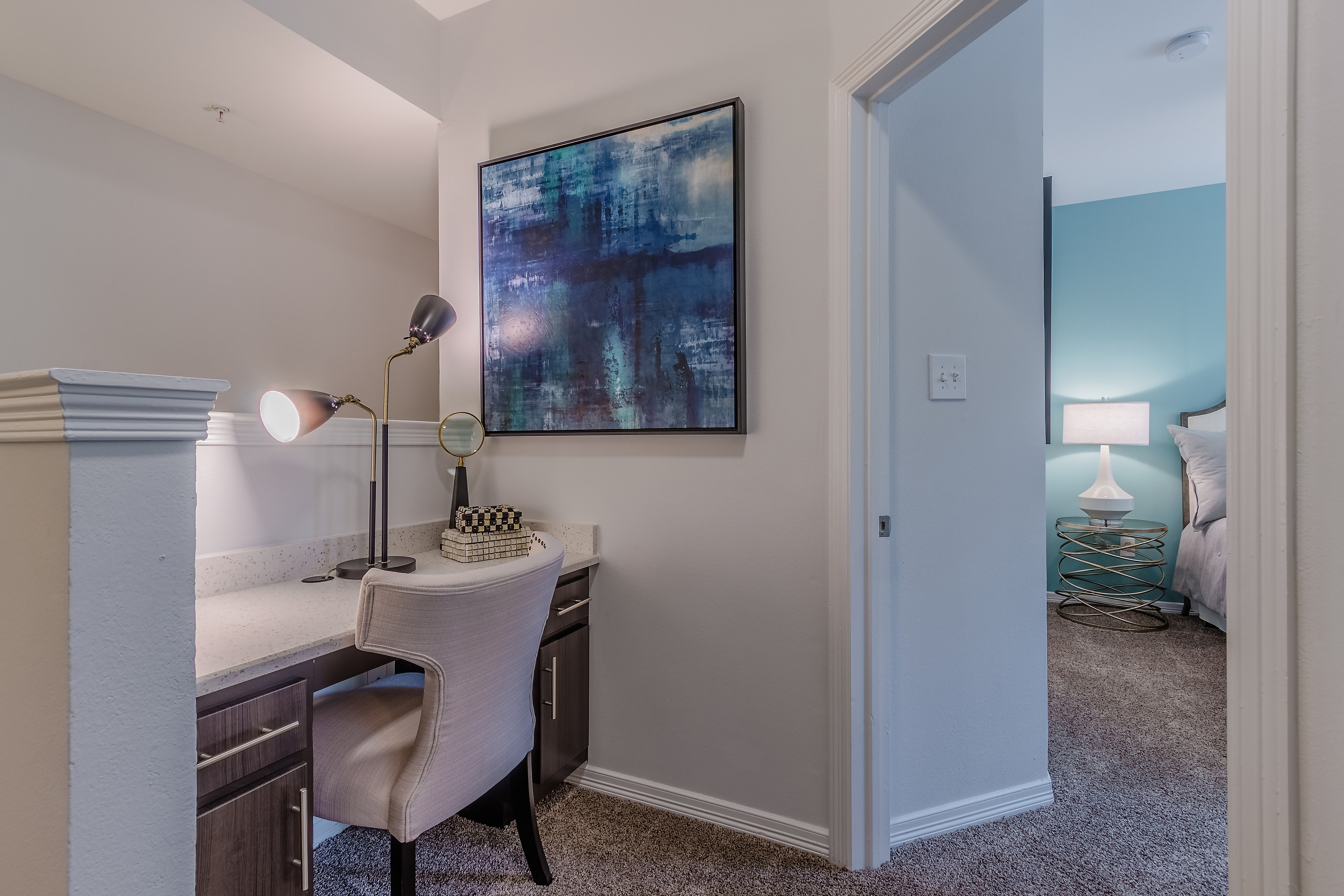 Chic apartment study nook with sleek desk setup, elegant artwork, and cozy bedroom glimpse, perfect for modern living.