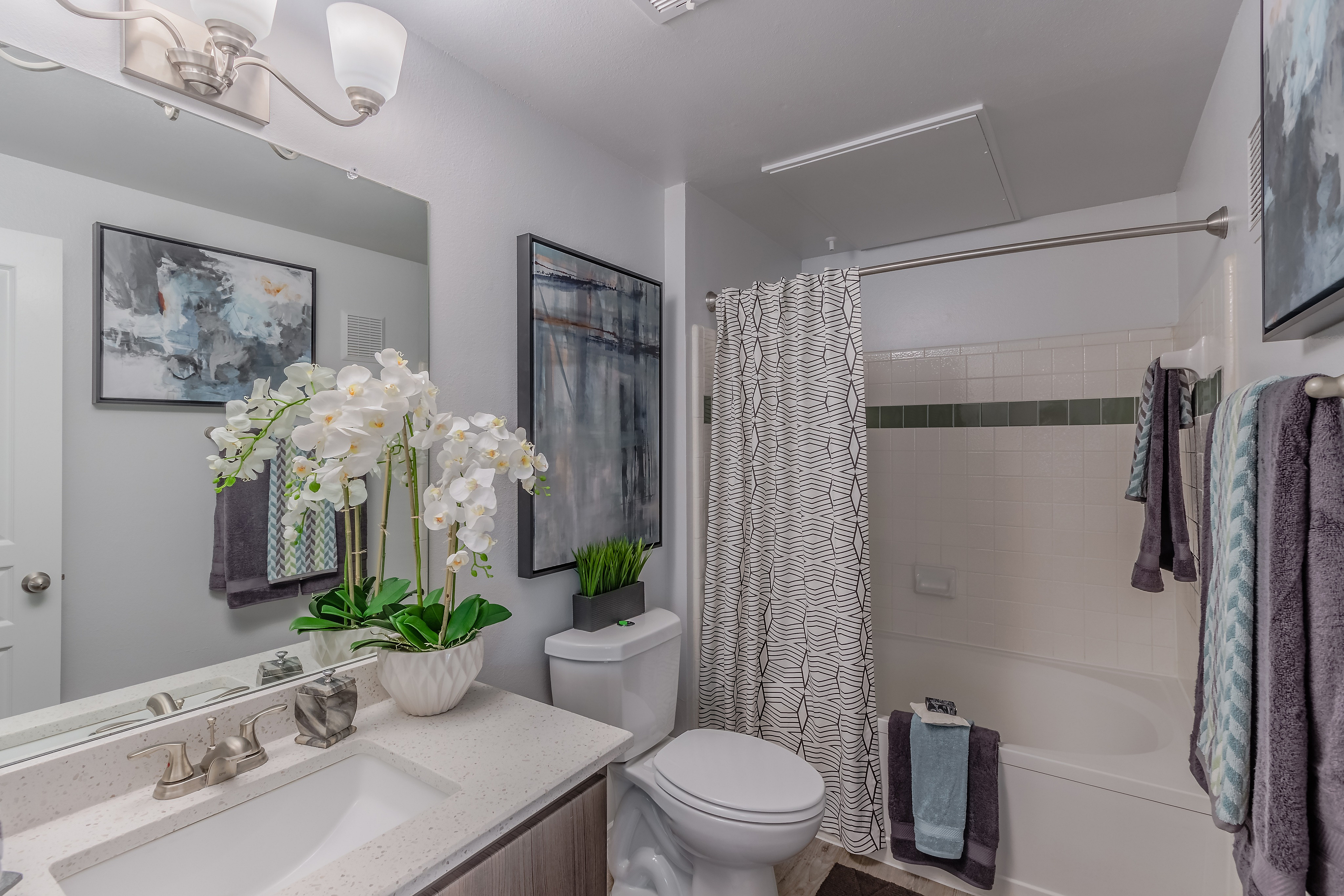 Elegant bathroom featuring modern fixtures, vibrant artwork, plush towels, and a stylish vanity with decorative orchids for a tranquil atmosphere.