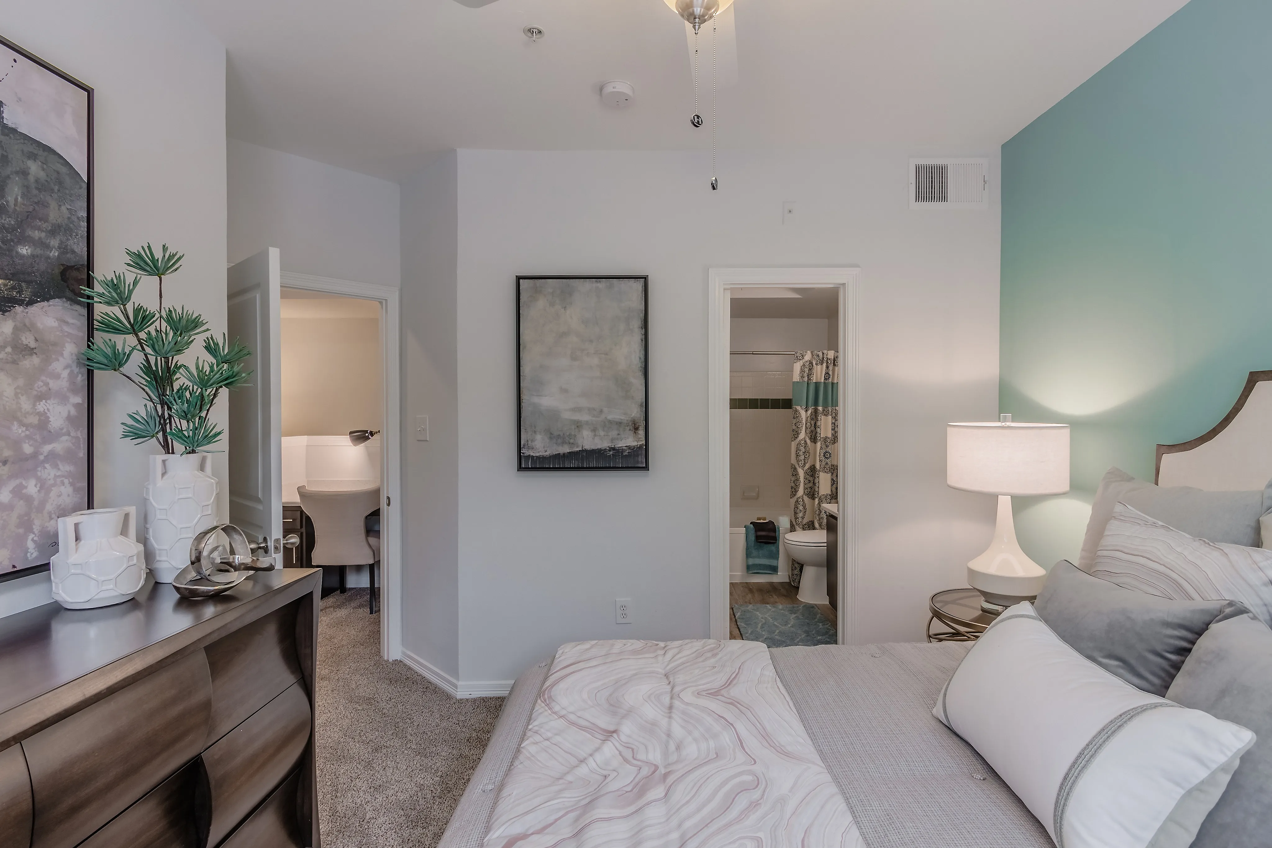 Inviting bedroom featuring a stylish bed with plush pillows, a modern nightstand with a lamp, and a glimpse into a chic bathroom.