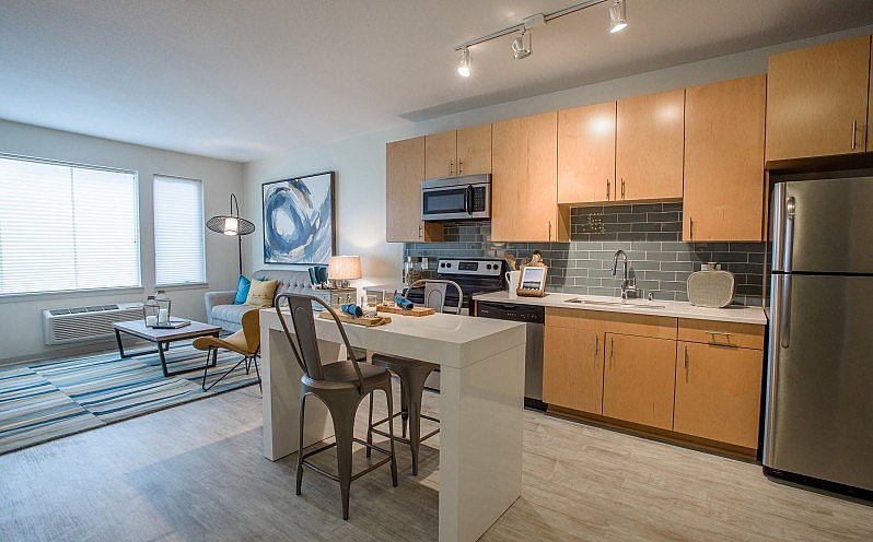 Modern apartment kitchen with sleek cabinetry, island dining, and open living space, featuring abundant natural light and contemporary decor.
