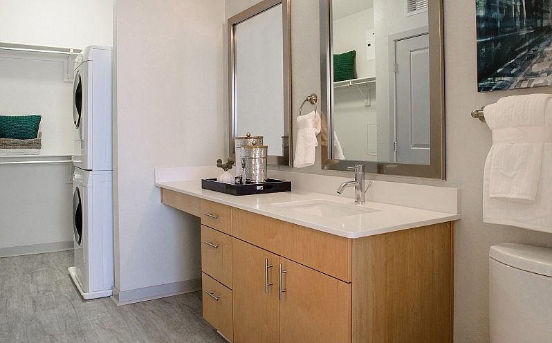 Modern bathroom with sleek wooden vanity, elegant mirrors, and in-unit laundry for convenient living.