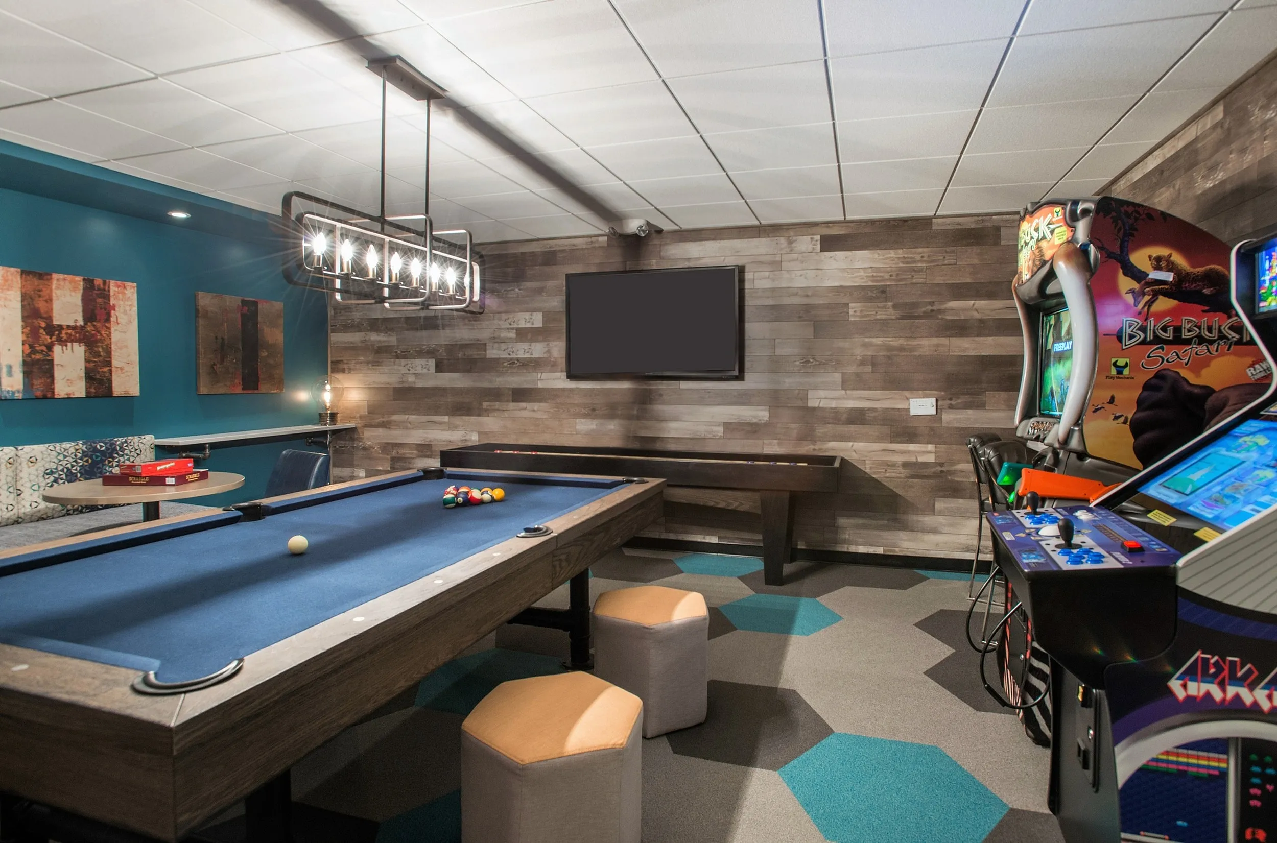Luxury entertainment room featuring a billiards table, arcade games, modern lighting, and cozy seating in a stylish wooden-accented space.