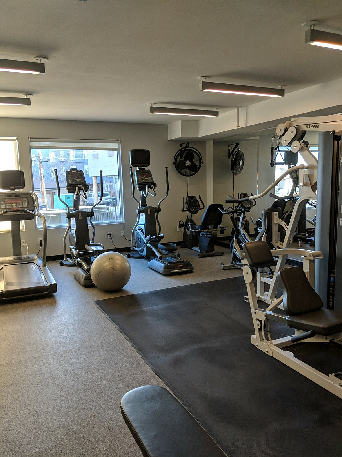 Bright and inviting apartment gym with modern exercise equipment, including treadmills, elliptical machines, and a weight station.