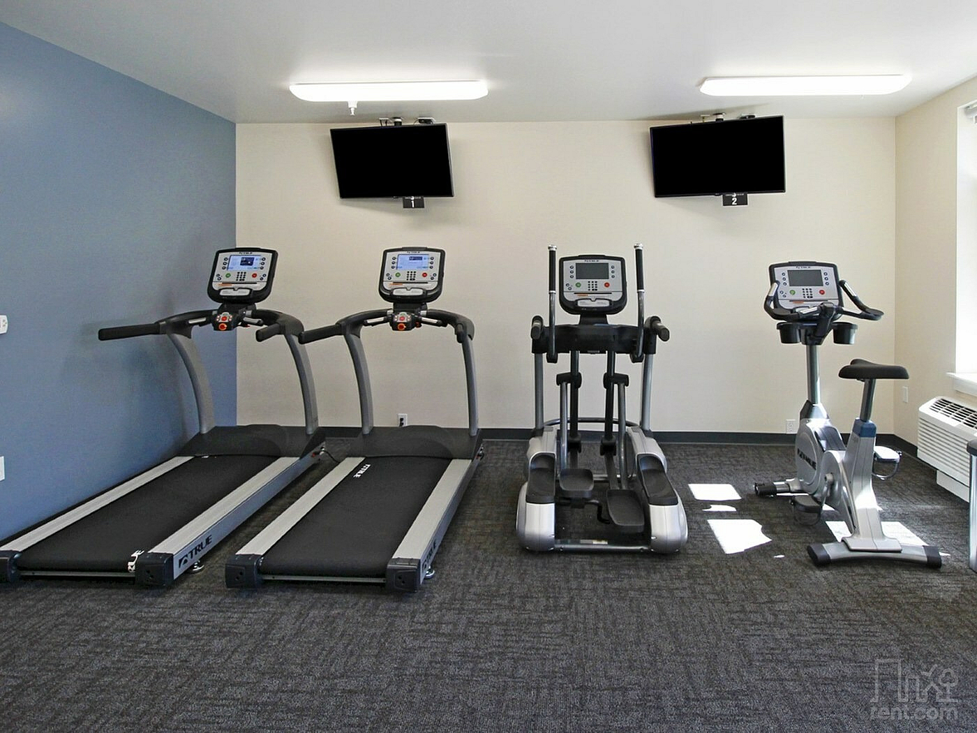 Modern fitness room featuring treadmills, elliptical machines, and stationary bike with sleek design and ample natural light.
