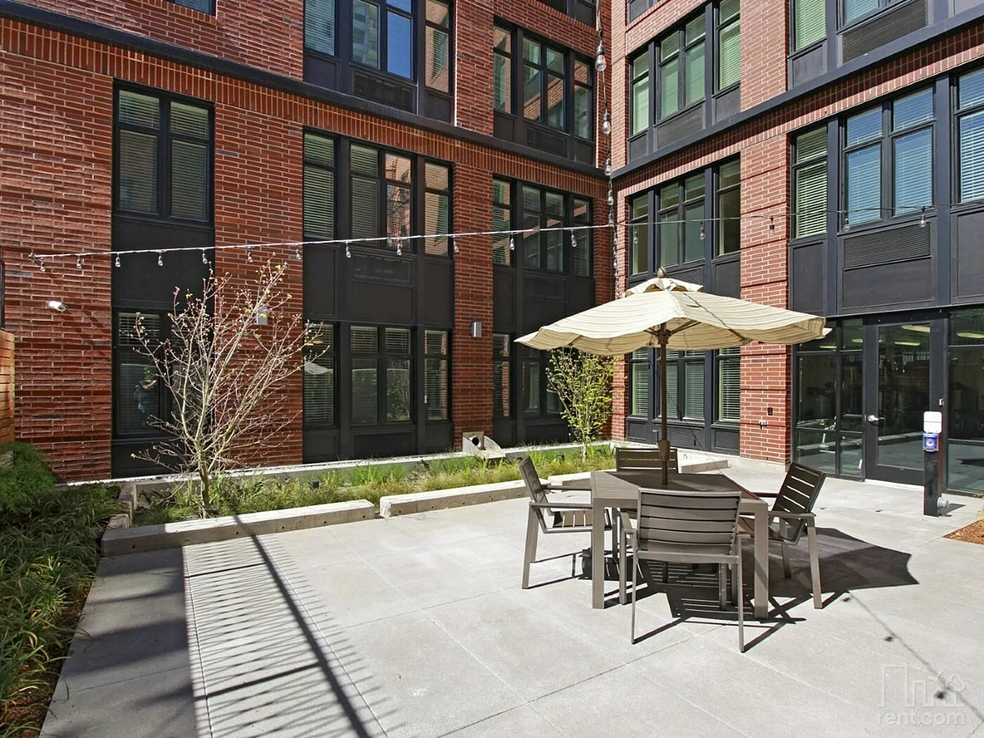 Modern apartment courtyard with stylish outdoor seating, sleek brick facade, and ambient string lights for a cozy atmosphere.