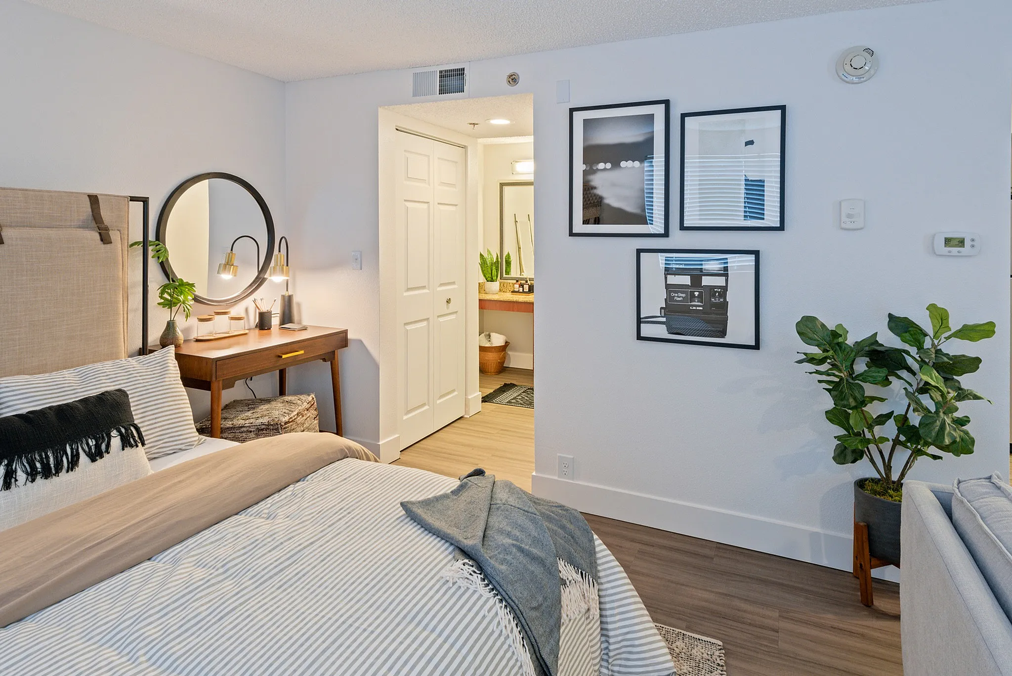 Charming bedroom with stylish decor, featuring a comfortable bed, wooden desk with modern lighting, framed artwork, and lush indoor plant, creating a cozy and inviting atmosphere.