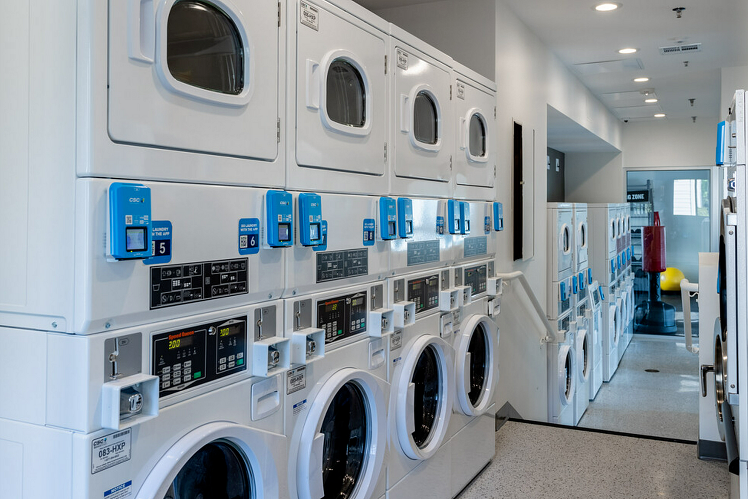 Modern apartment complex laundry room featuring state-of-the-art washers and dryers with digital controls, sleek design, and ample folding space.