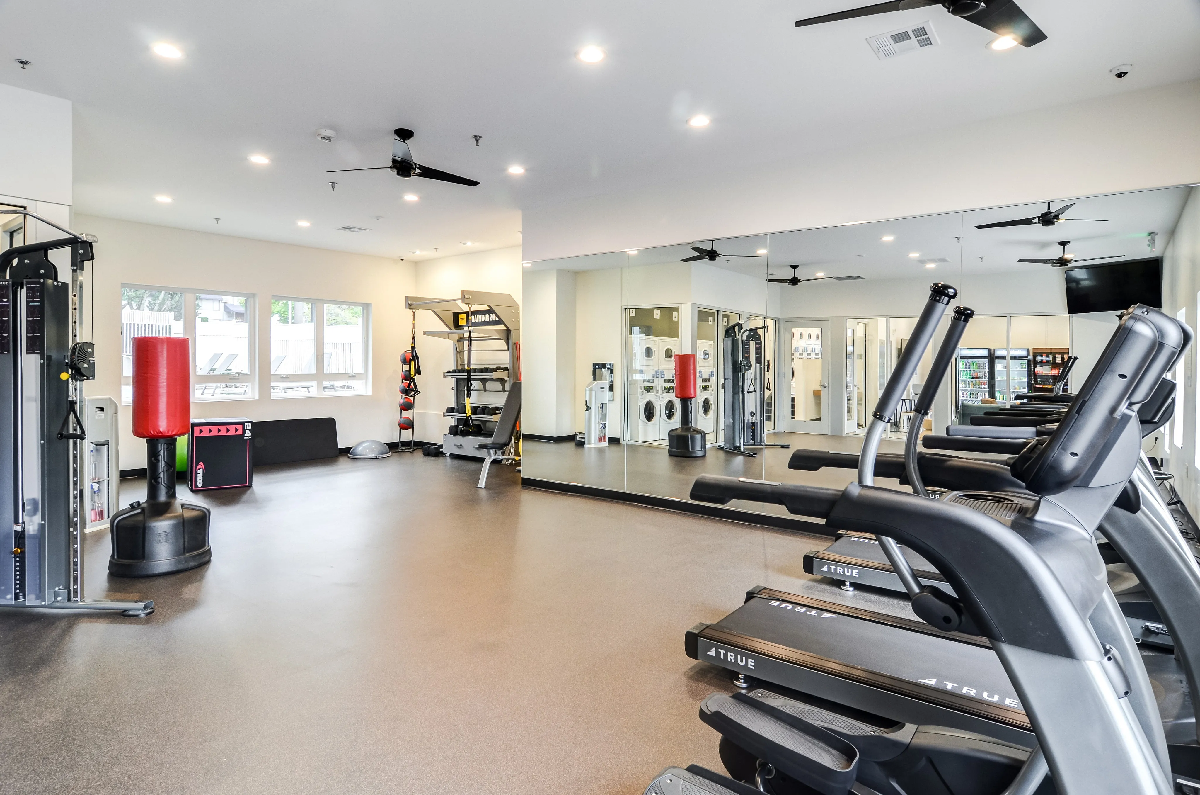 Modern gym with state-of-the-art equipment, including treadmills, punching bags, and weight machines, in a spacious, well-lit environment.