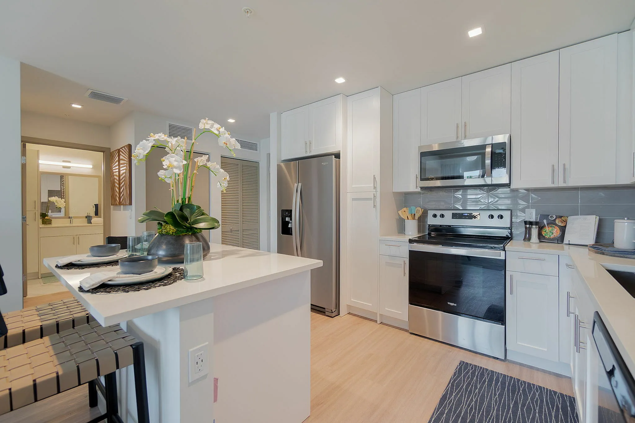 Modern kitchen with sleek stainless steel appliances, elegant white cabinetry, and a chic breakfast bar adorned with fresh orchids.