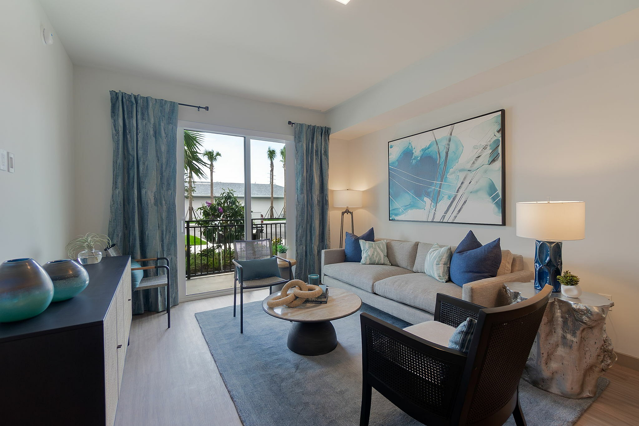 Inviting living room with elegant decor, featuring a cozy sofa, abstract artwork, and bright natural light from large windows overlooking a lush garden.