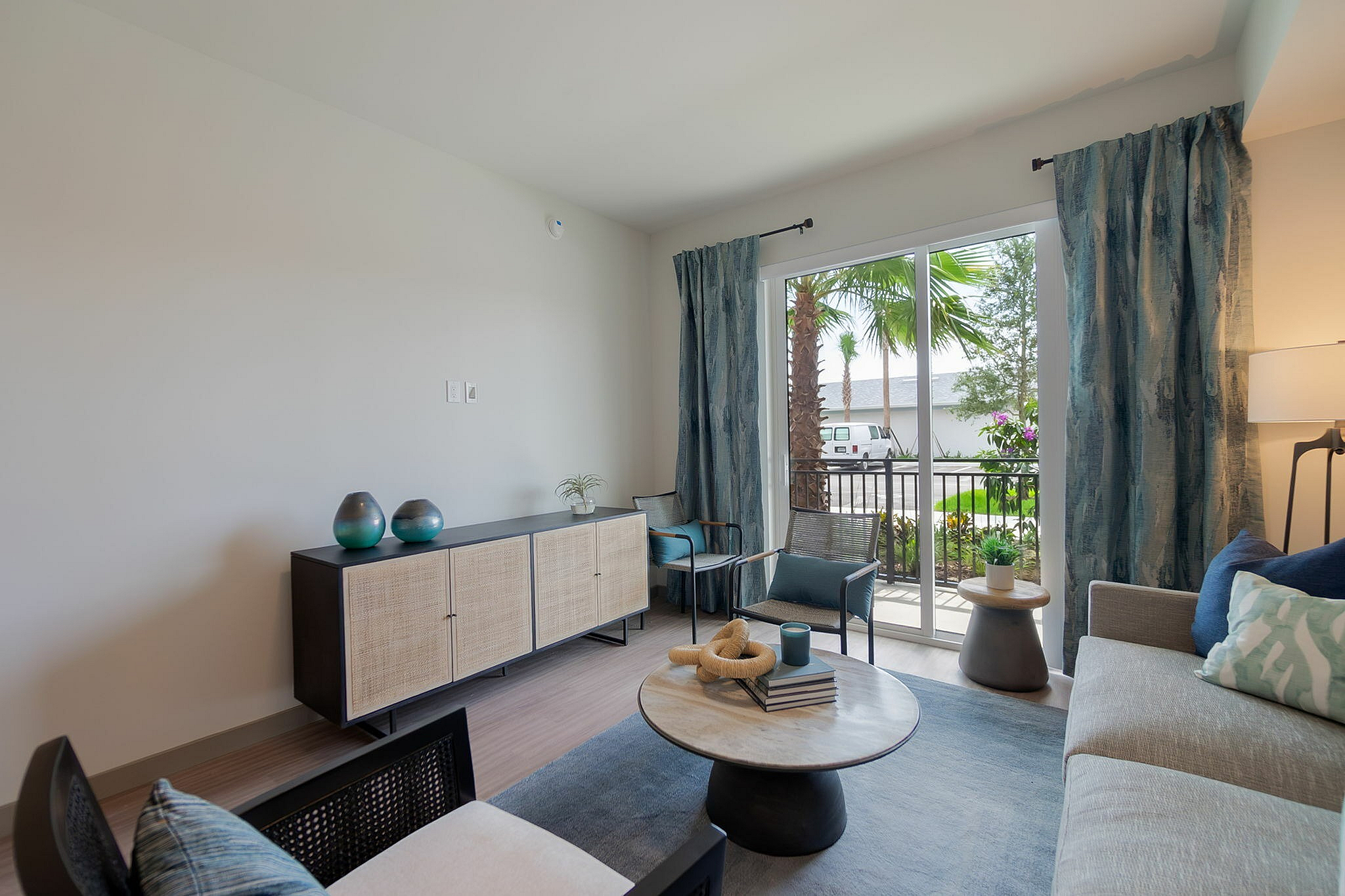 Bright and modern living room with stylish decor, cozy seating area, and a scenic view of lush greenery through glass doors.