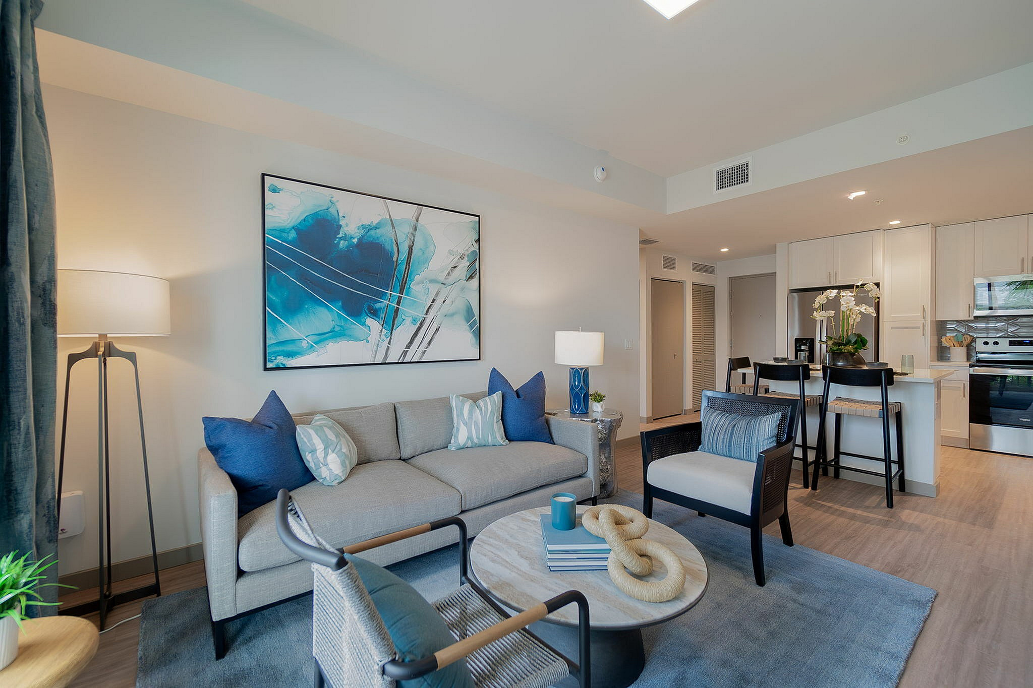 Bright and modern open-concept living space with elegant decor, featuring a cozy seating area, sleek kitchen, and stylish bar stools.