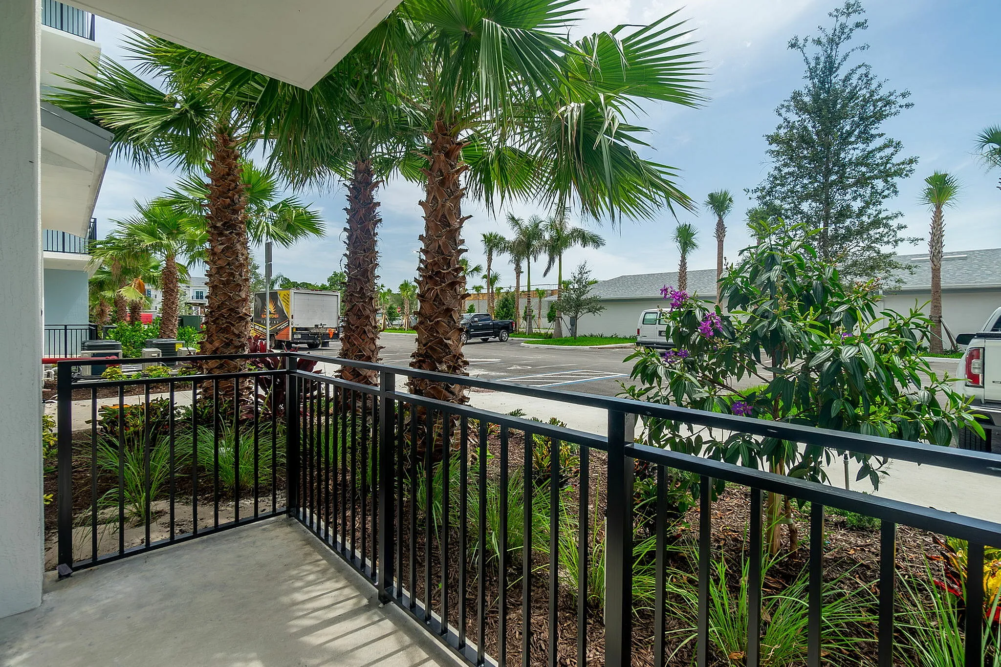 Relaxing balcony view from an apartment, featuring lush palm trees and vibrant landscaping for a tropical ambiance.