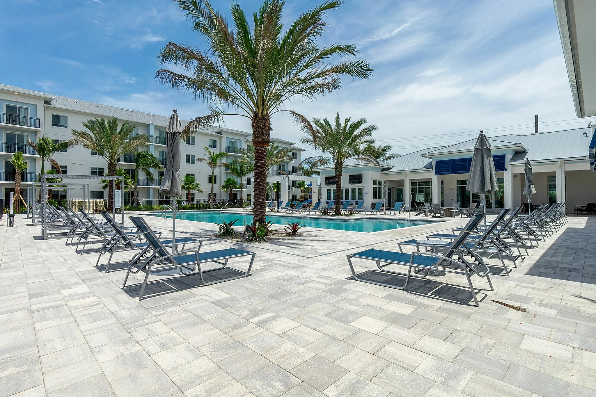 Luxurious apartment complex poolside with palm trees, modern sun loungers, and a serene atmosphere under a bright blue sky.