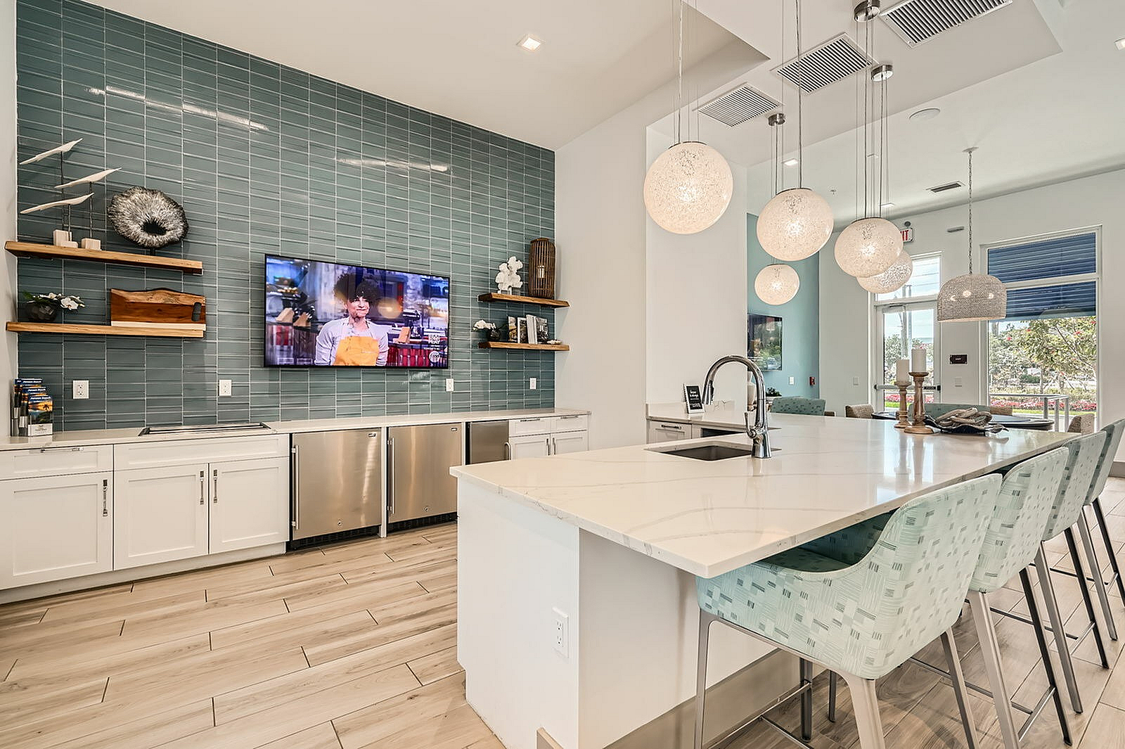 Elegant modern kitchen with a sleek island, designer pendant lights, and a wall-mounted TV, perfect for entertaining.