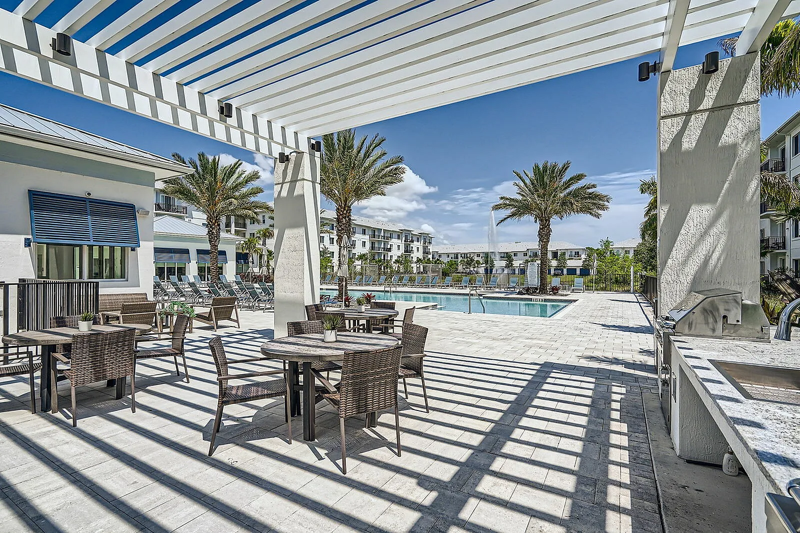 Luxurious outdoor pool area with stylish seating, palm trees, and modern architecture under a clear blue sky.