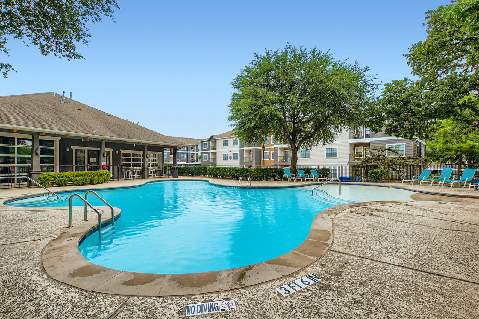 Inviting community swimming pool surrounded by lush greenery and modern apartments, perfect for relaxation and leisure.