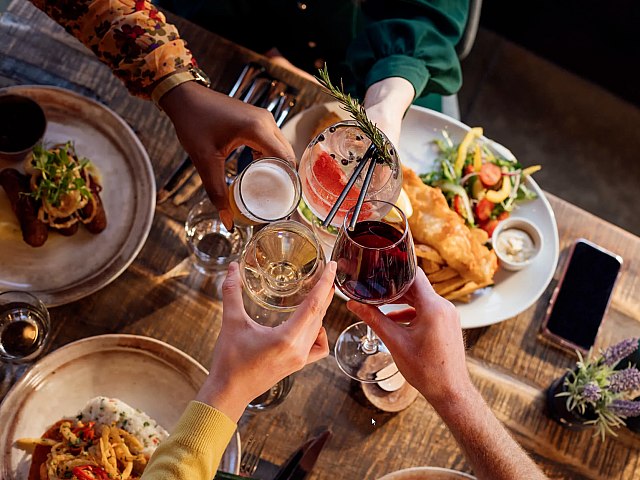 Top view of a lively dining table with various dishes and people toasting with drinks, creating a celebratory atmosphere.