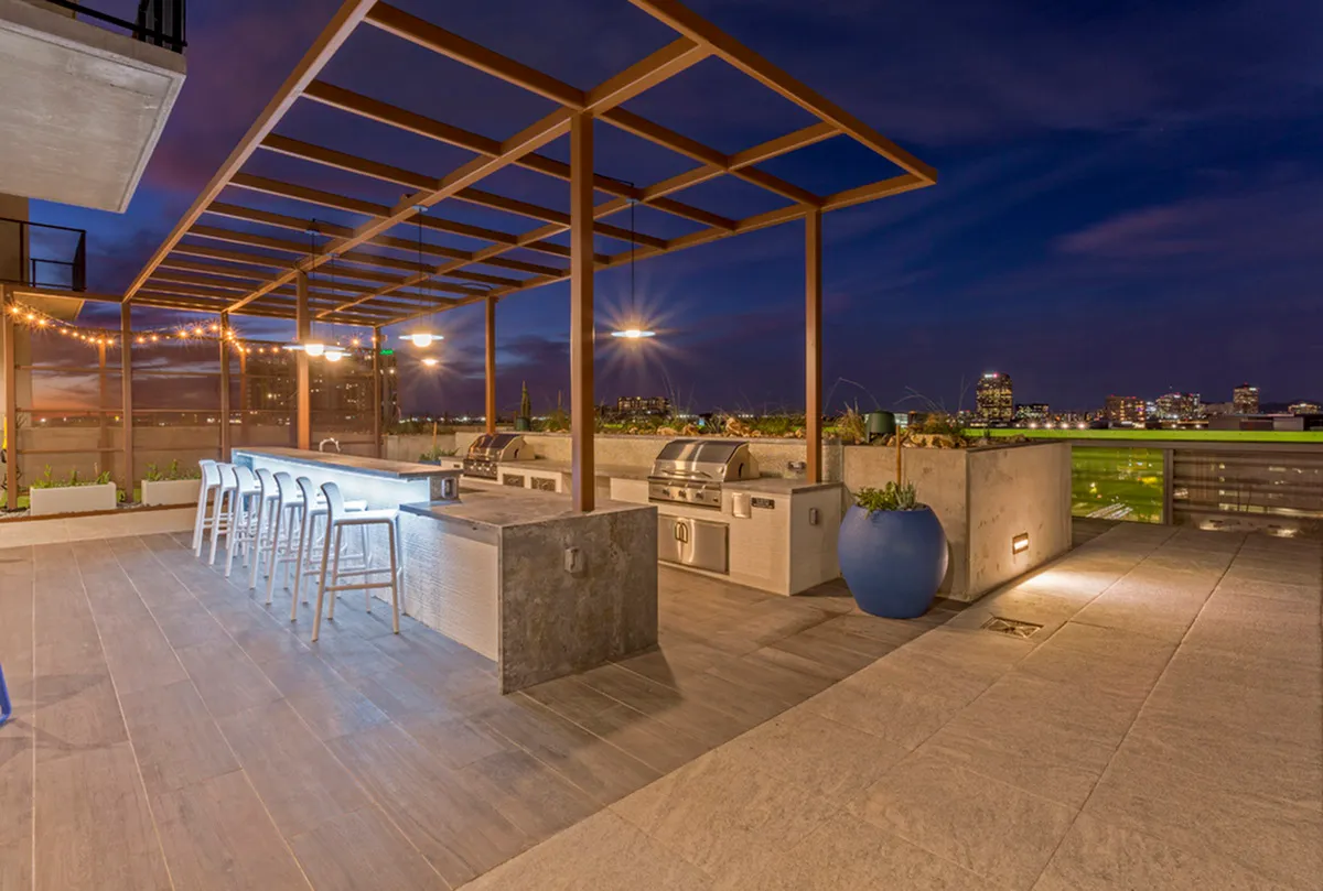 Elegant rooftop lounge with modern pergola, outdoor grill station, and city skyline views at twilight.